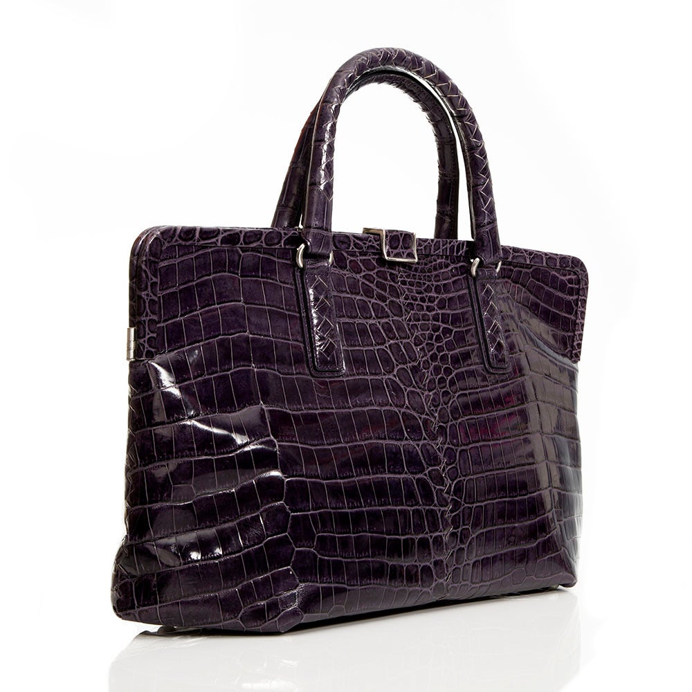 Featuring an exquisite crocodile skin in eggplant purple, this handbag from Bottega Veneta is complimented by silver hardware on the handles and clasp and a hexagonal opening. This piece has a large interior along with an internal zip-compartment