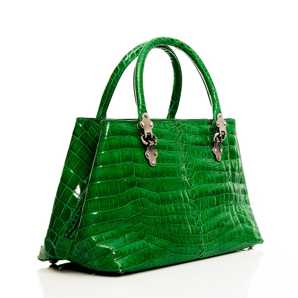 Featuring an exquisite crocodile skin in a Shamrock green, this handbag from Bottega Veneta is complimented by silver hardware on the handles and zip. This piece has a large internal compartment and features a vanity mirror crafted in the same