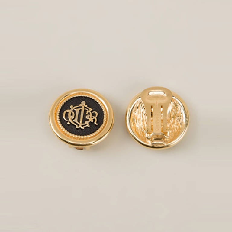 Christian Dior Vintage Logo Emblem Earrings.  	
Black and gold plated metal logo emblem earrings from Christian Dior Vintage featuring a clip-on fastening. Combining black and gold-toned metal, this piece exudes an edgy appeal as well as a classic