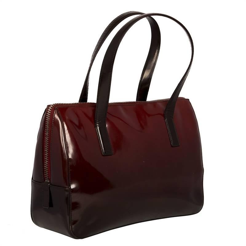 This Prada handbag features a beautifully burnished leather in a deep, rich shade of burgundy. Timeless and subtle, its facade is embossed with the Prada logo. Offset with dark brown leather straps and silver-tone hardware, the bag has a Prada