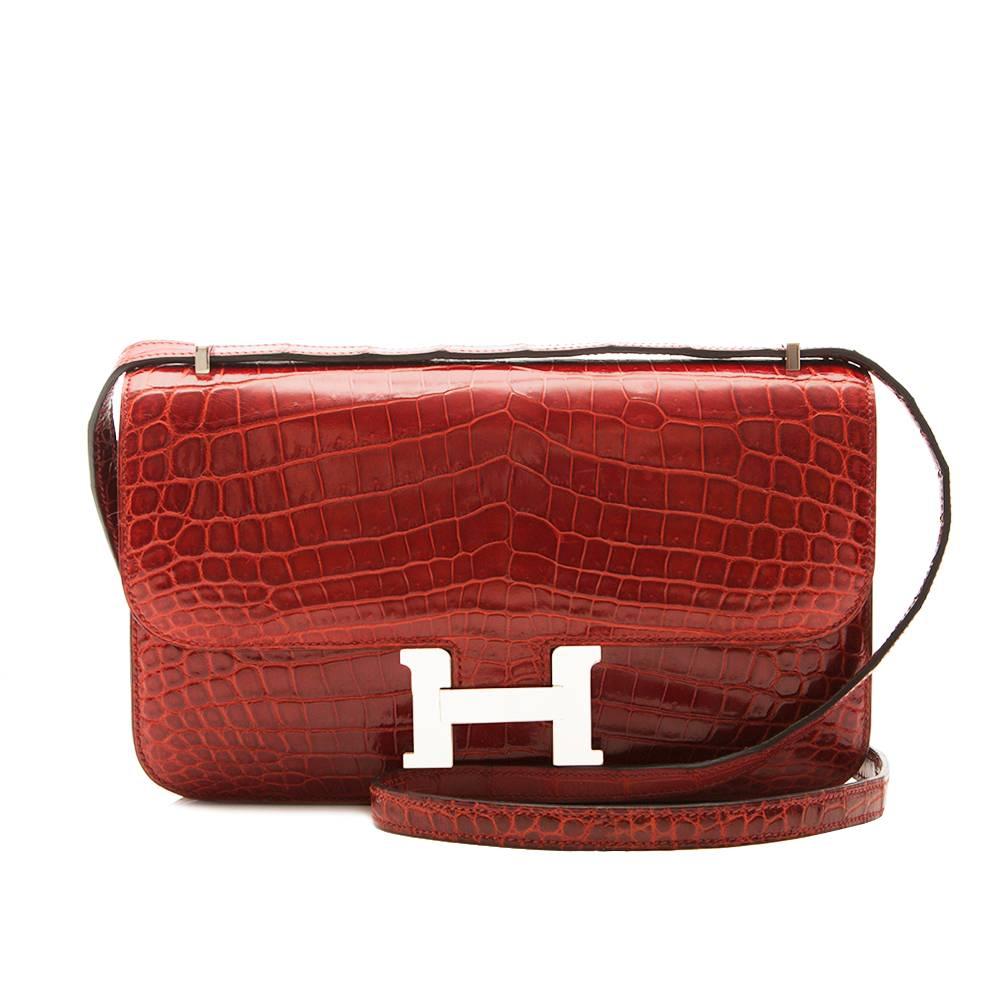 This is a Hermes Rouge H Constance Elan 25cm is crafted from highly precious Porosus crocodile in a vivid red shade. Offset with palladium-plated hardware, its slender body is adorned with the brand's signature 'H' snap-lock fastening, a rear pocket