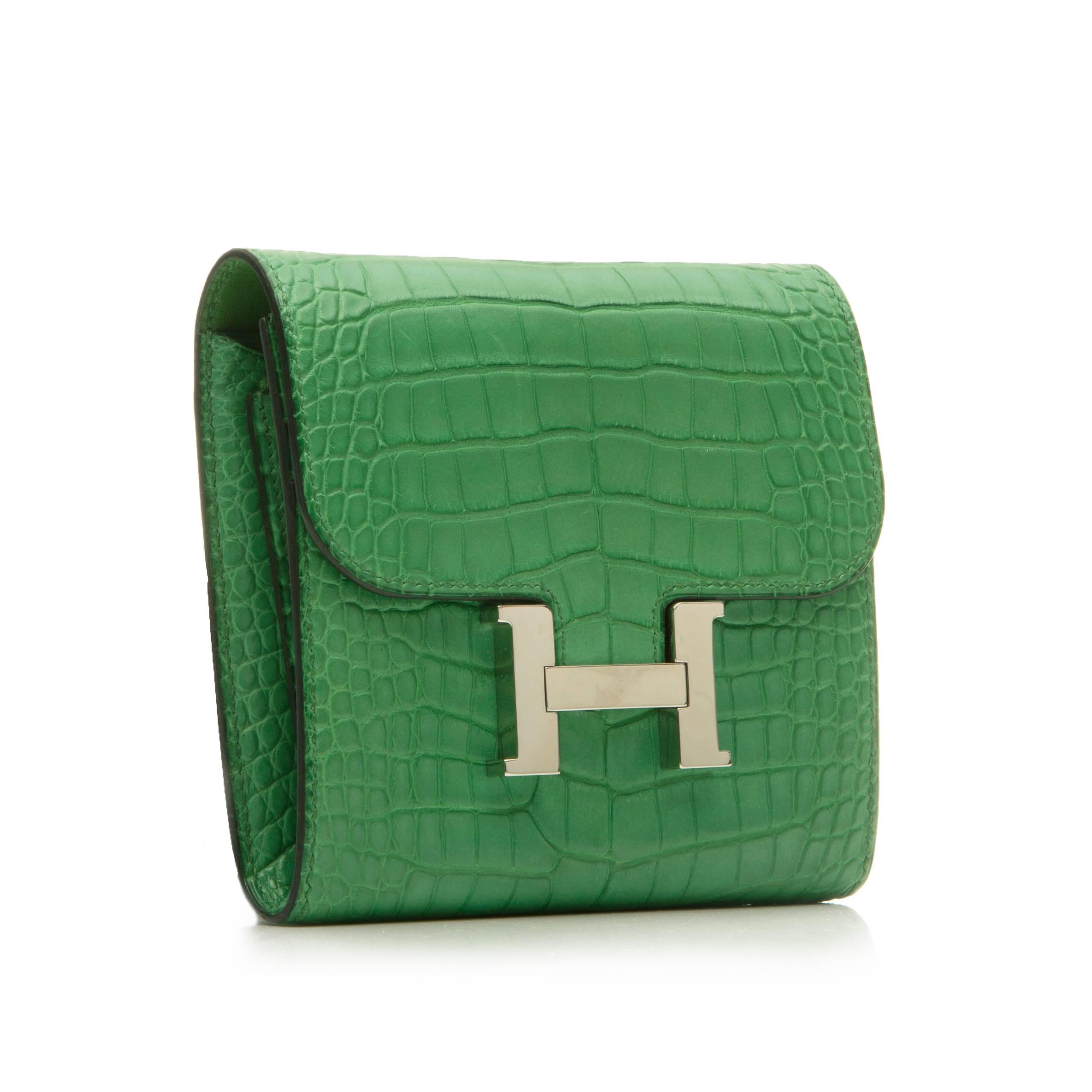 A bold design for organising monetary essentials, this Hermès Constance wallet is crafted in a Cactus green alligator skin offset with silver-plated palladium hardware. Featuring the iconic Hermès Constance logo fastening, a back slip pocket,