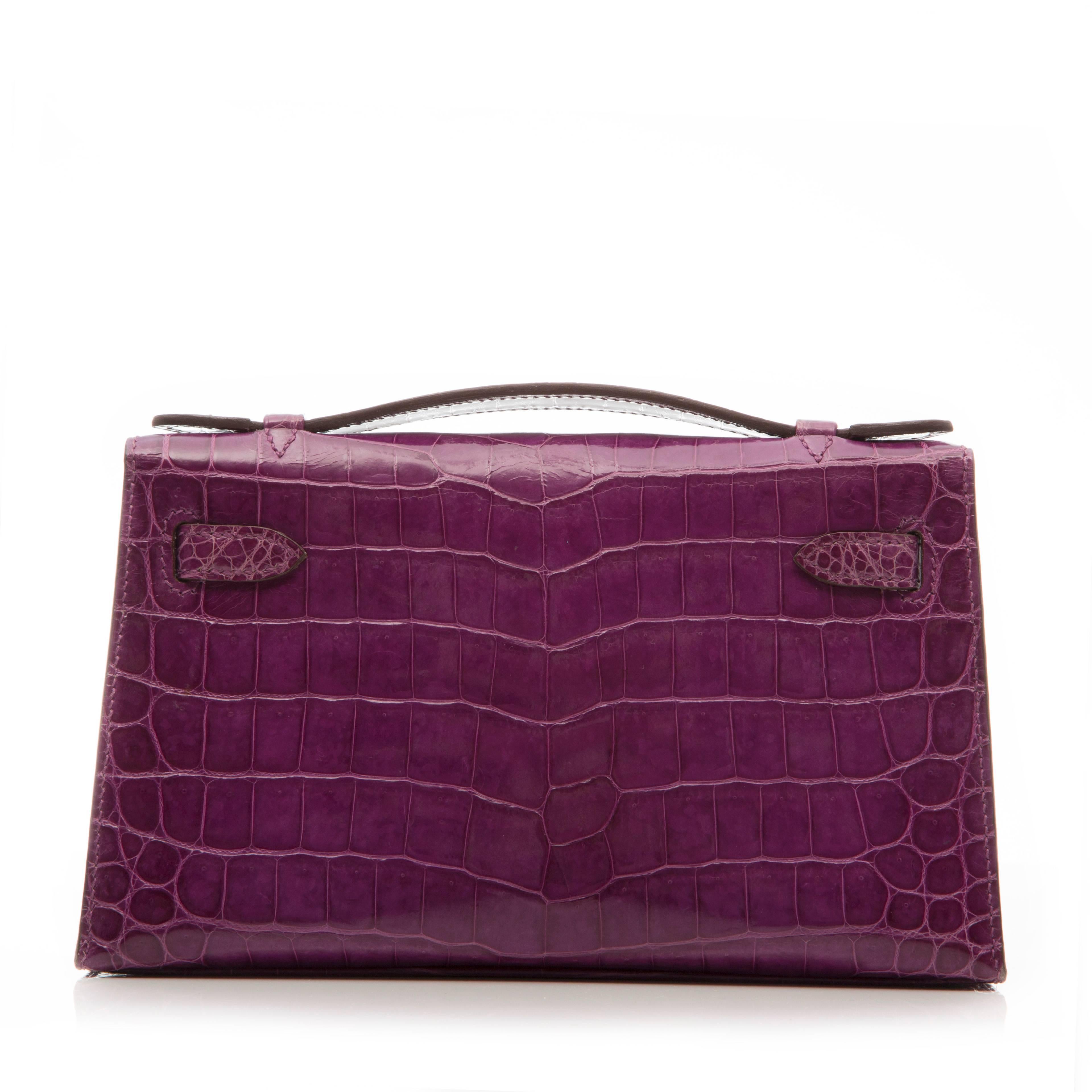 While miniature in size, the Hermès Kelly Pochette is filled with the signature details of its big sister, the Kelly tote. This Hermès Kelly Pochette is crafted from a glossy Niloticus Crocodile in fuschia, offset with pale gold-tone hardware. It
