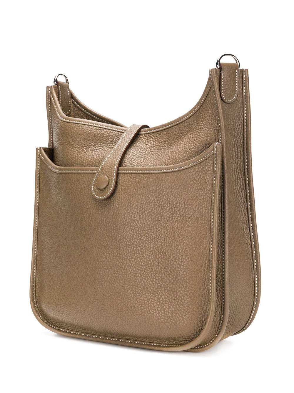 Crafted in a smooth Taurillon Clemence leather, this Evelyn bag by Hermes remains stylish, functional and contemporary in a refined saddle-like shape with a perforated H logo decorating the front. The bag displays a grained texture with an