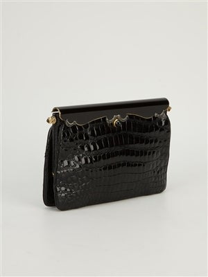 With echoes of Art Deco, this vintage clutch is crafted in crocodile leather, and finished ornately with embossed metal and an onyx-like stone clasp. Executed in a sleek shape for an effect that is sultry and darkly glamorous. Its interior is lined