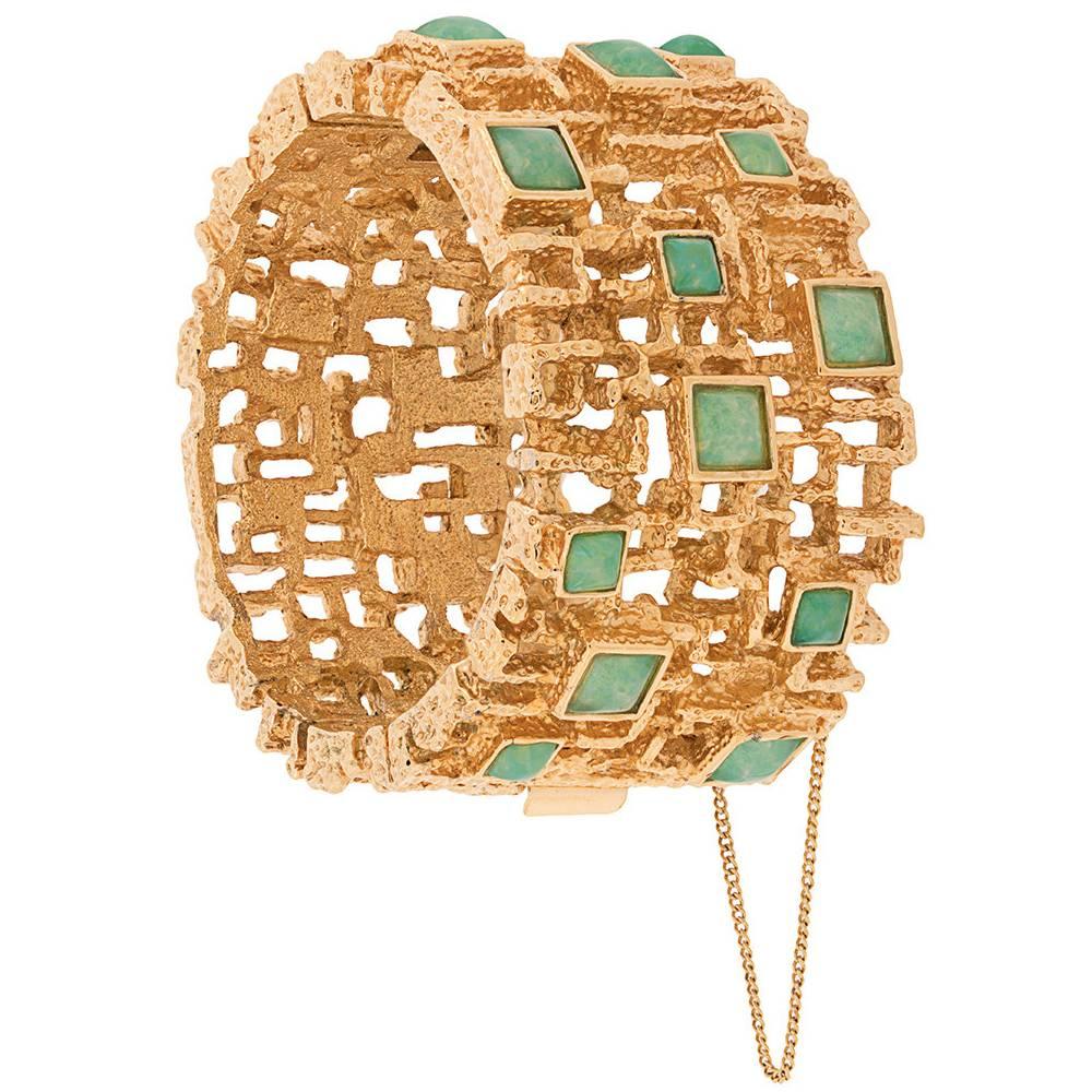 A 1960s gold-tone bracelet featuring green glass stones and a hinge fastening with chain.

Colour: Gold, green

Material: Gold-plated metal, glass

Measurements: Circumference: 17.5cm, width: 4cm

Pre-owned, excellent condition.