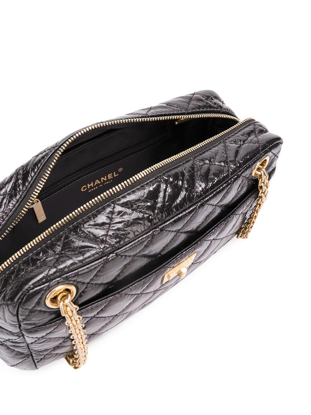 Crafted in black aged and distressed calfskin leather, this timeless camera case by Chanel features a distinctive quilted design and patent finish, two gold-tone mademoiselle chain shoulder straps and the turn lock fastening designed by Coco Chanel