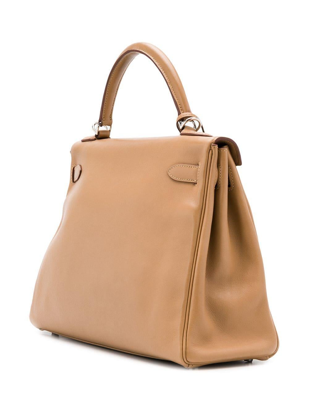 Diese klassische 32-cm-Handtasche von Hermès Kelly ist elegant aus geschmeidigem Swift-Leder in einem schönen und erdigen Biskuitbraun gefertigt. Das komplizierte Design wird durch die ikonischen versilberten Palladium-Hardware der Marke akzentuiert