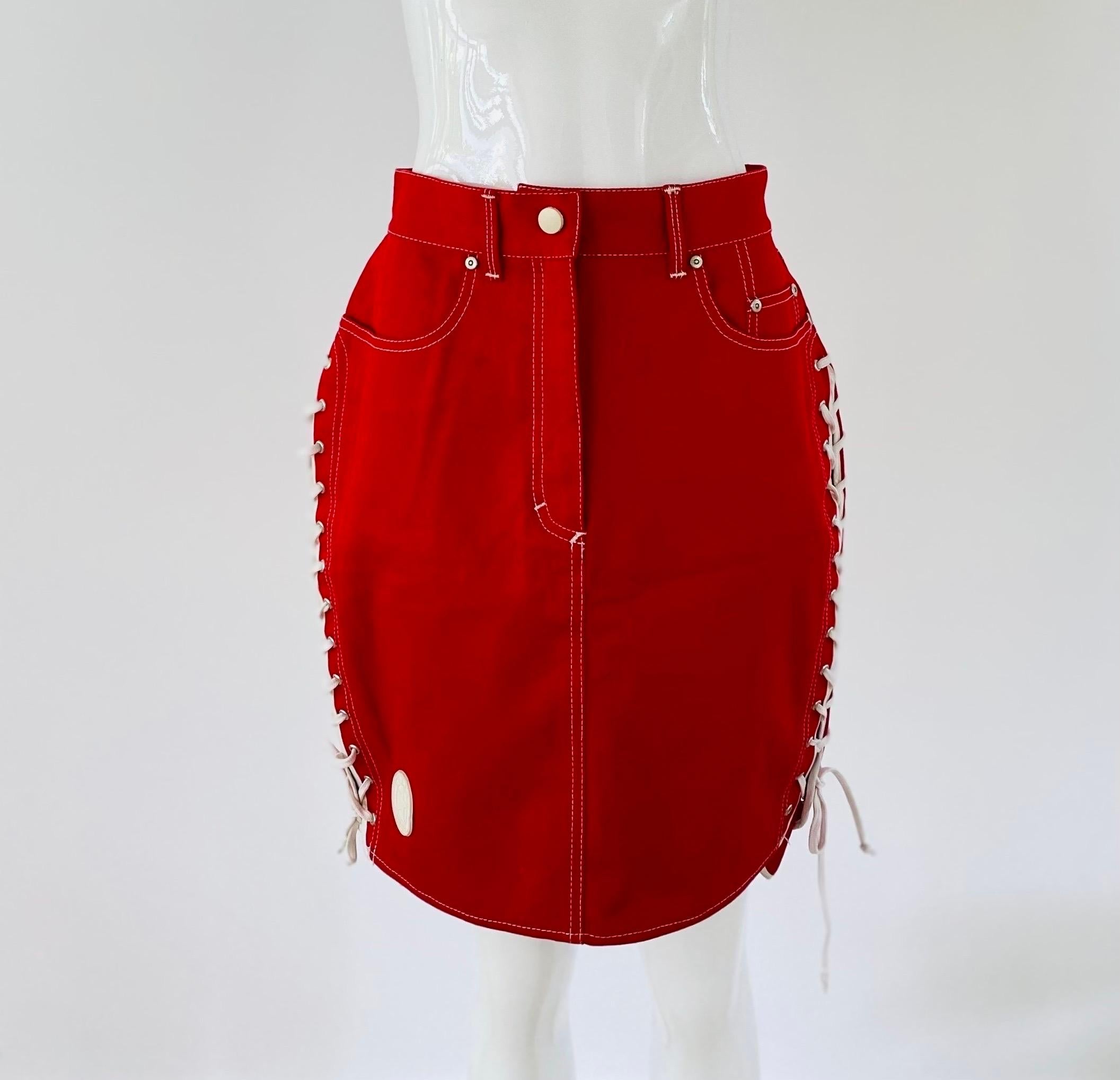 1980s Gaultier Junior above the knee red skirt with white stitches. It resembles a pair of converse with a star patch on the front bottom right corner and laced up shoelaces on each side. Functional pockets on the front and back. White snap button