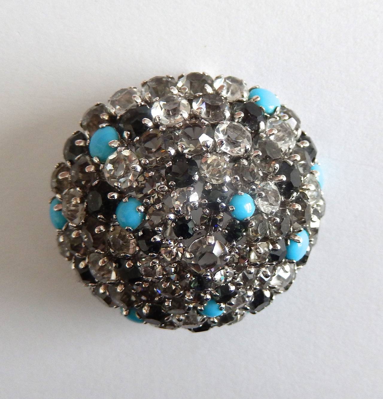 A vintage Dior brooch that combines grey, clear and black faceted crystals with faux turquoise gemstones. A beautiful, domed design.  Dior jewelry from this early period is scarce. Pin could also be worn on a chain.  Marked:   Christian Dior 1961