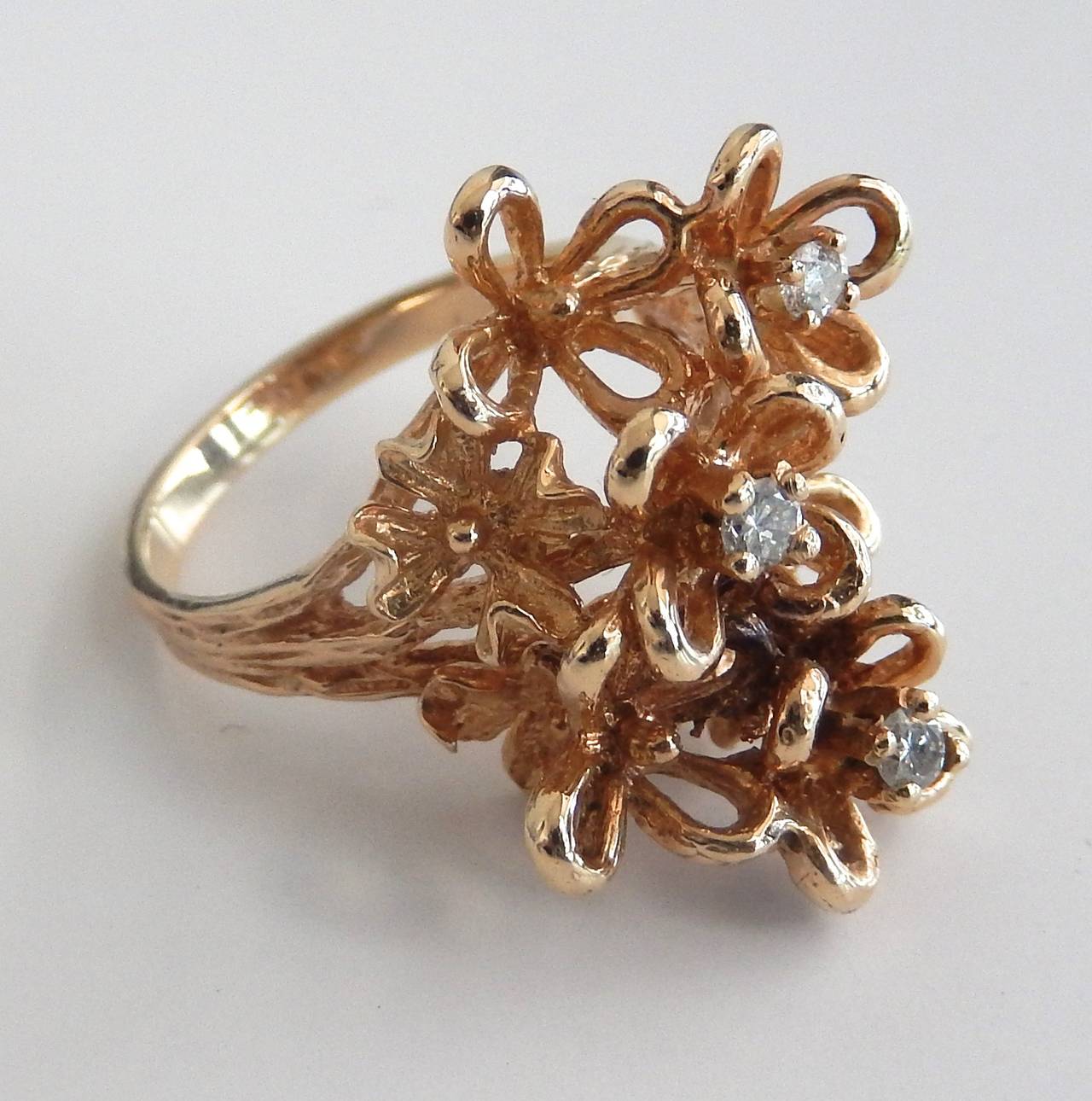 A sculptural ring of three diamonds and 14K textured gold with a stylized floral motif setting.  A graceful and lively design.  Ring size:  7