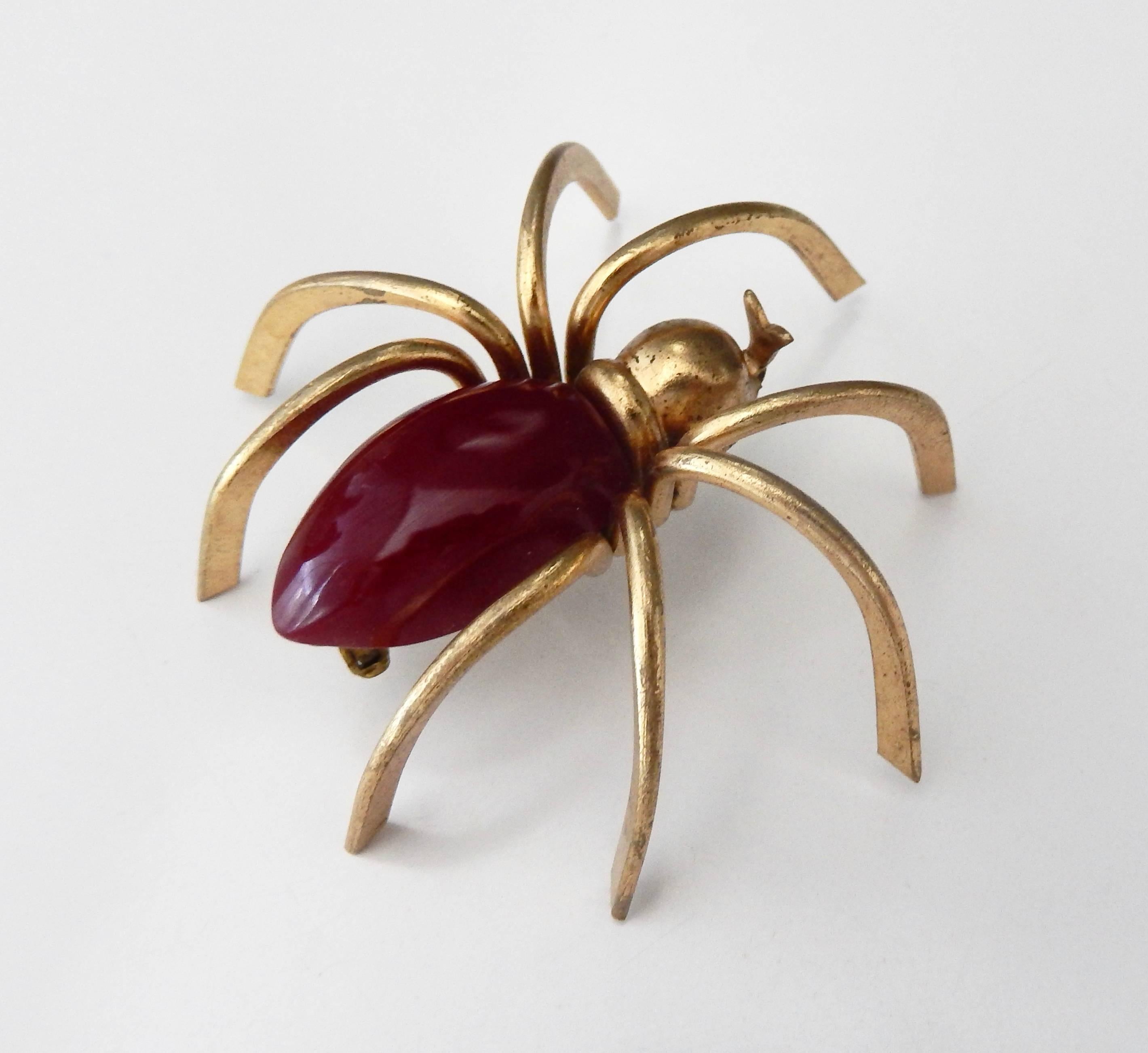 A whimsical three-dimensional gilt metal spider pin with a burgundy red bakelite body from the 1930s.  In very good condition.  A classic, scarce example of American Art Deco costume jewelry.  (Note that in bright sunlight the bakelite takes on a