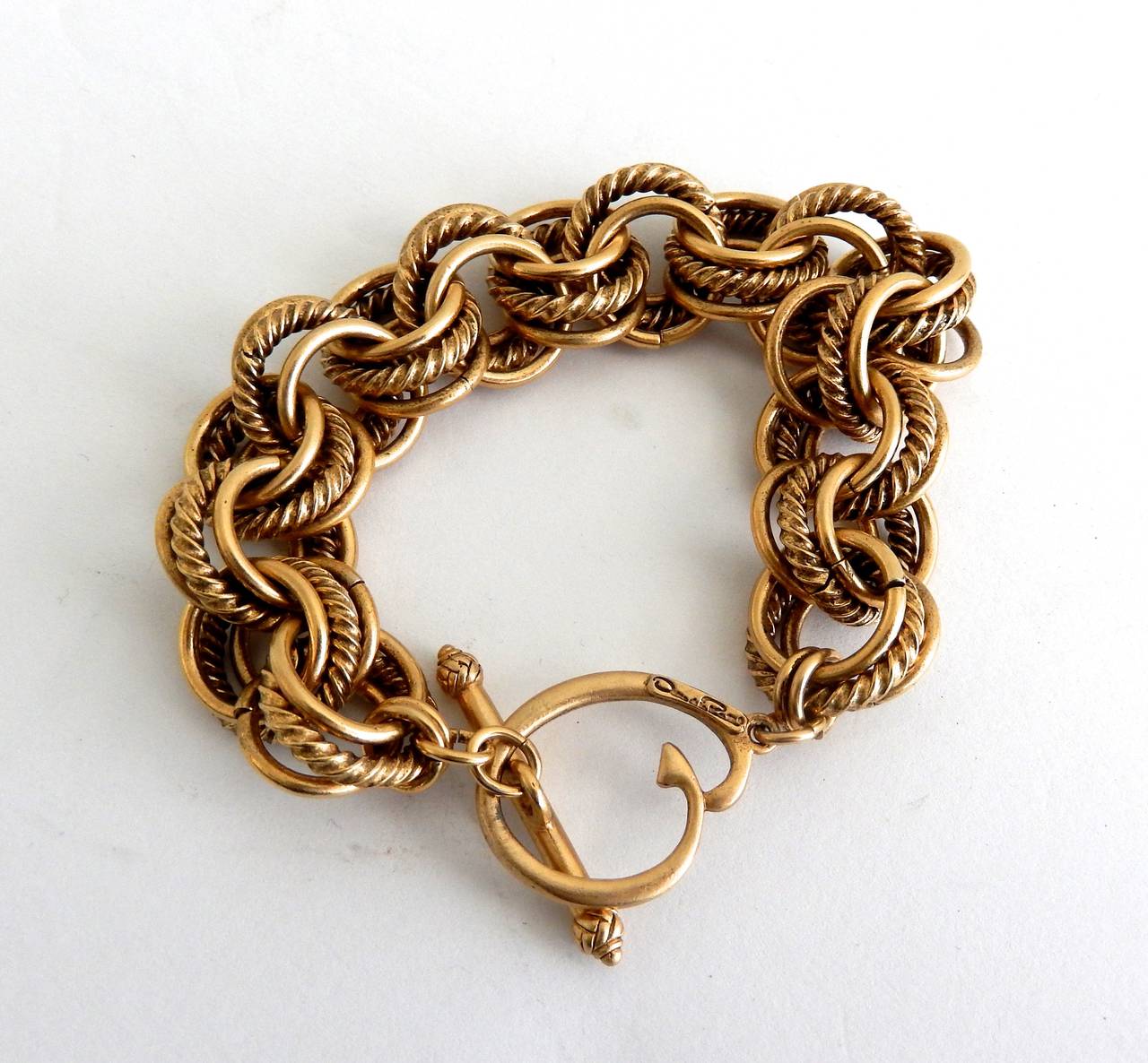 A gold tone link bracelet combining different textured hoops by Oscar de la Renta. Decorated toggle clasp. Signed.