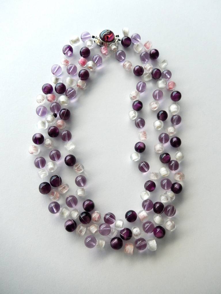 A three-strand beaded necklace in hues of amethyst ranging from light violet to deep purple.  The necklace is signed on the clasp and has the signature black bead. In Ancient Greek amethyst means 