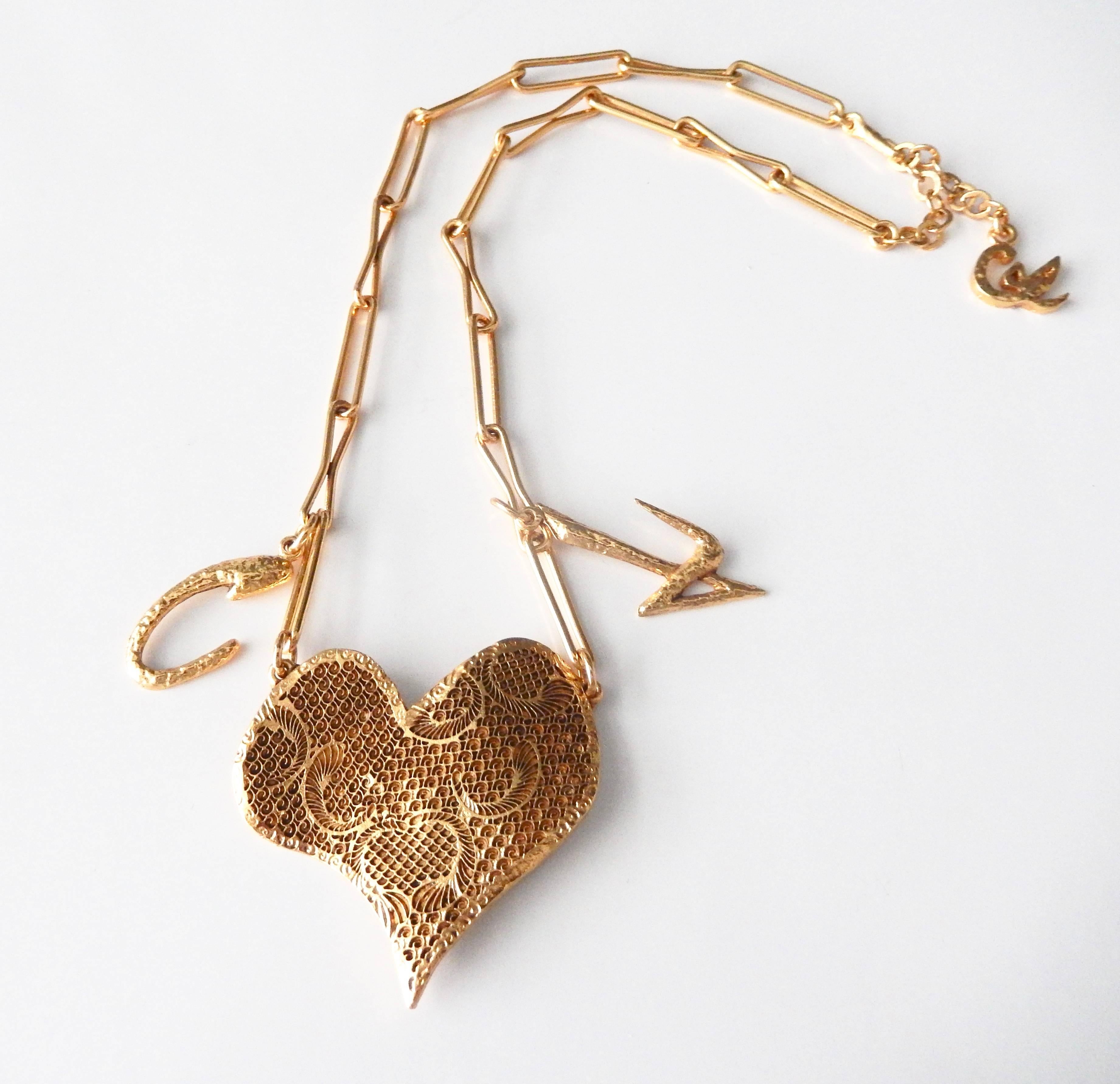 A textured mesh, gilt-metal heart pendant by Christian Lacroix.  The delicate, open link chain also includes two Lacroix signature charms, 