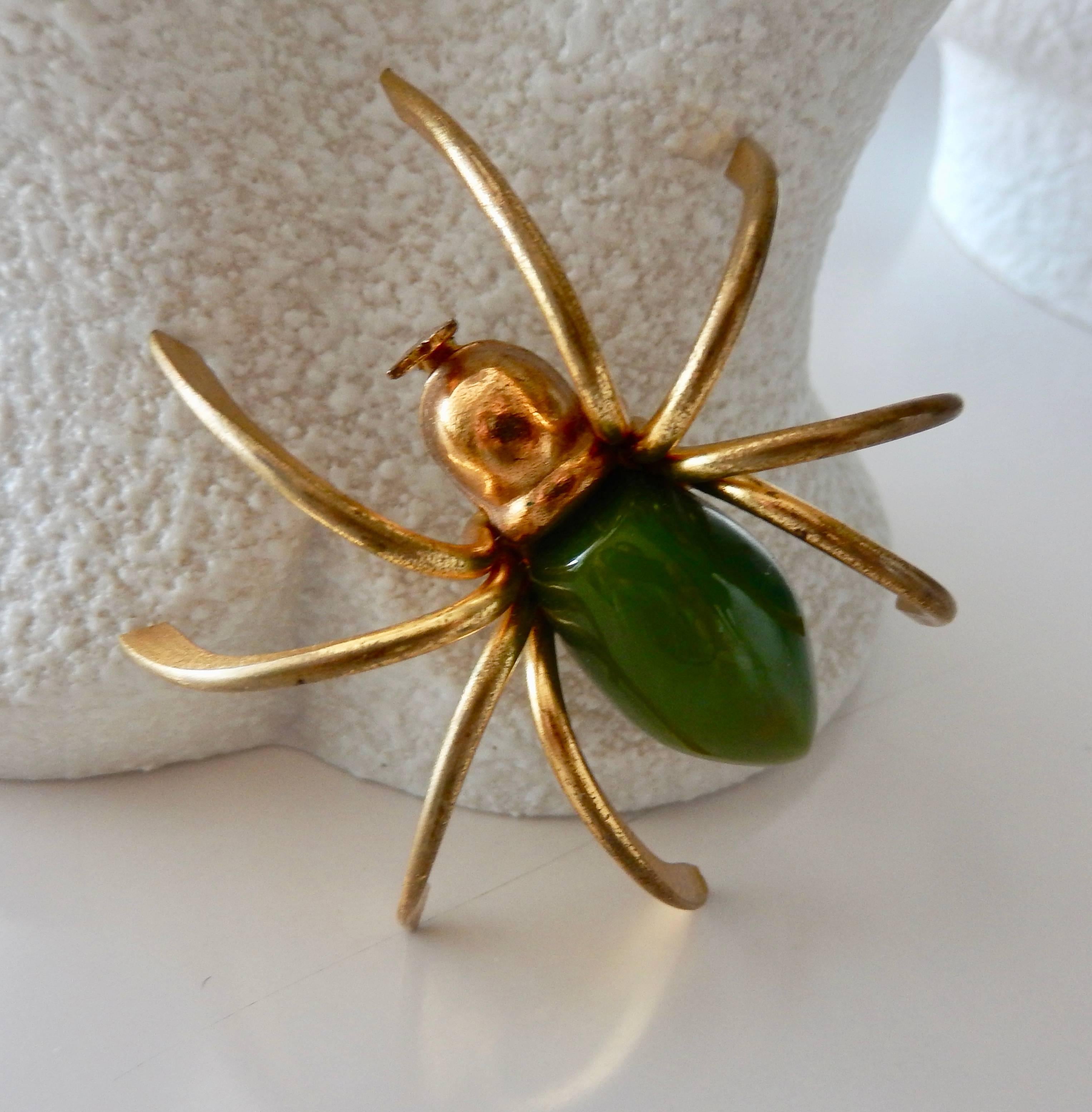 A whimsical three-dimensional gilt metal spider pin with a green bakelite body from the 1930s. In very good condition. A classic, scarce example of American Art Deco costume jewelry.  The only spider you would want to accompany you to a holiday