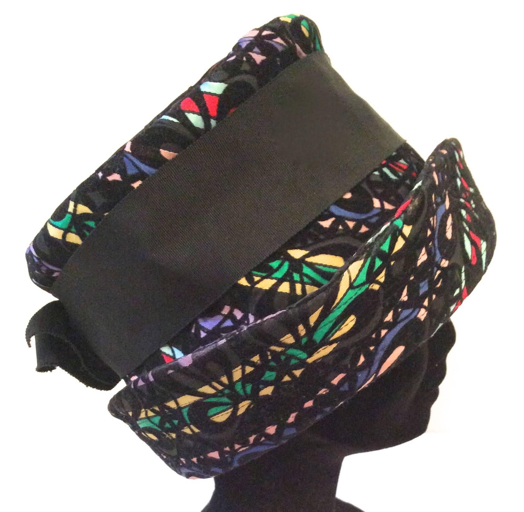 This fabulous multi-colored wide brimmed hat is from the late 1950's, early 1960's. It is in excellent condition. The hat encompasses a multi-colored striped background layered with black felt. Floral, geometric design. The beautiful underlying