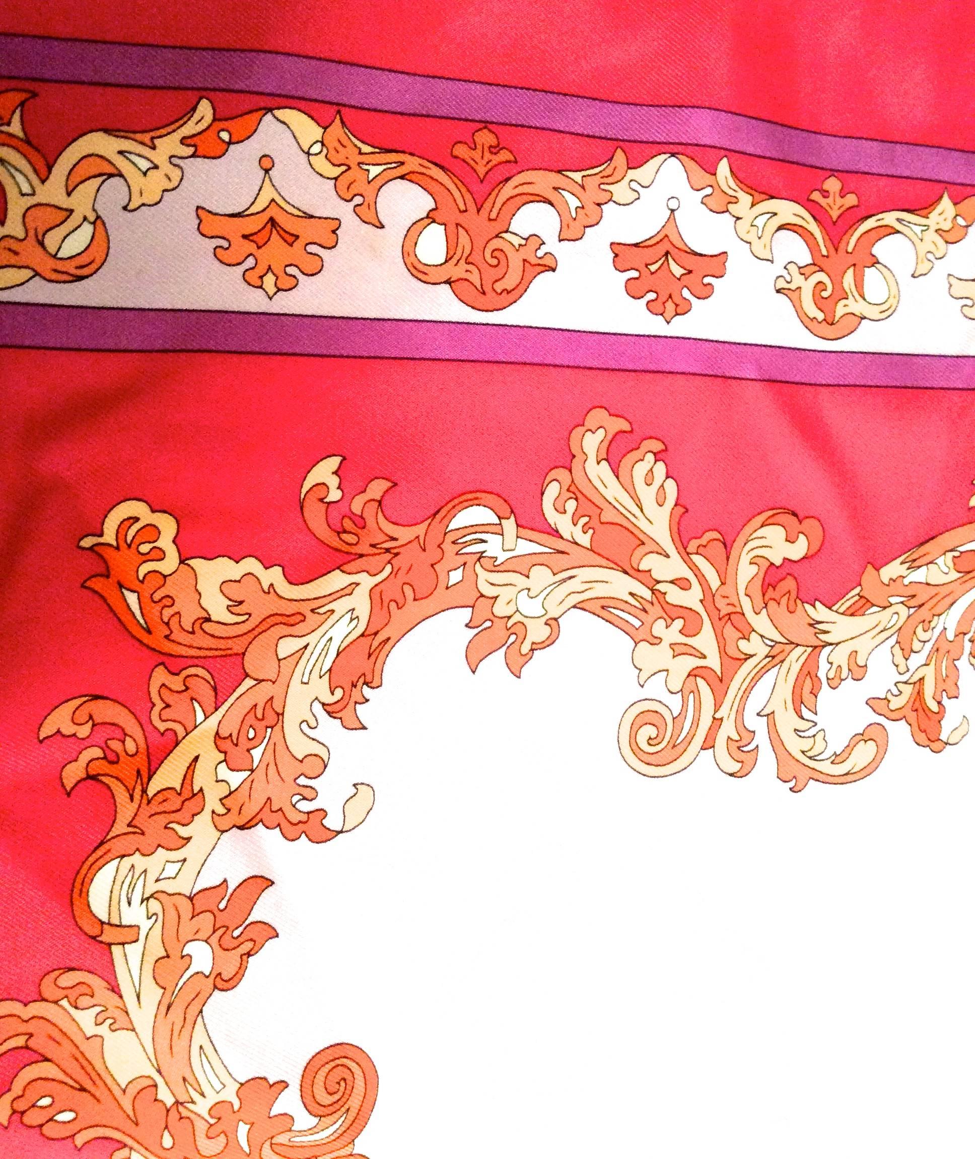 Presented here is a new Emilio Pucci silk scarf. The scarf is a combination of shades of red, purple, orange, and tan. The design is an ornate curved leaf-shape design separating the main colors of the scarf. There is a diamond / ovular shape in the
