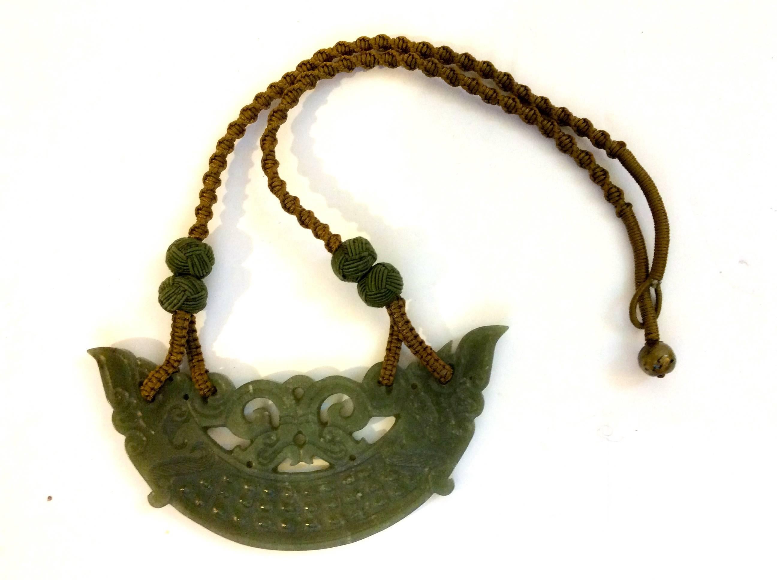 Presented here is an elaborate green jade necklace. The necklace is comprised of an curved section of green jade that has been intricately cut by hand. The necklace has a woven silk cord neck band. The necklace has a woven loop closure at the back
