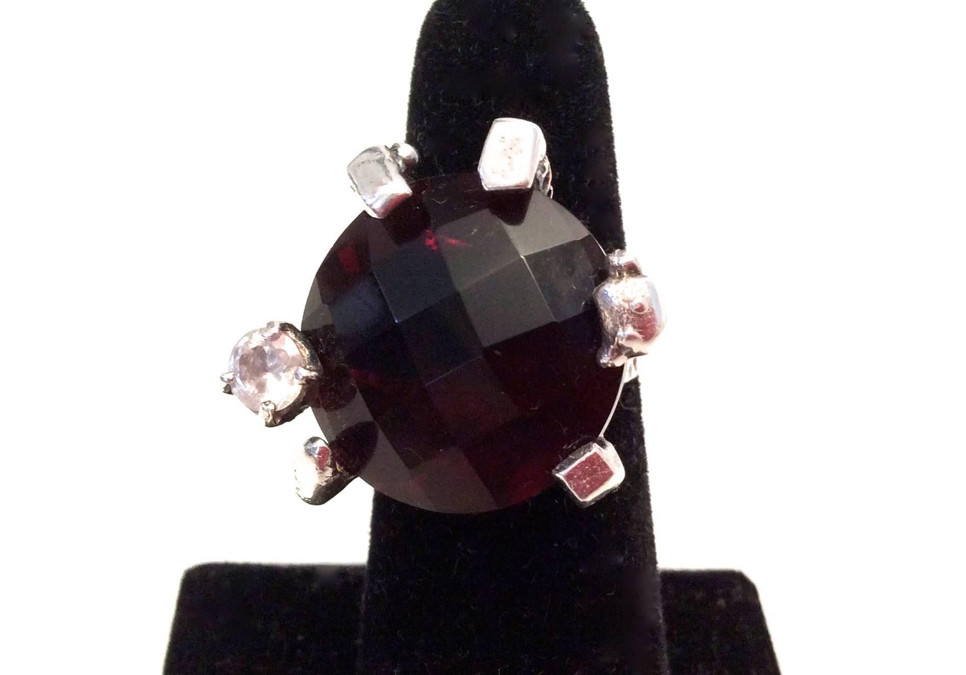 Presented here is a Christian Lacroix sterling silver ring. The setting appears to be a design of geometric roots framing the side of the ring with a large brown gem stone in the setting. There is another single clear stone on the top of the