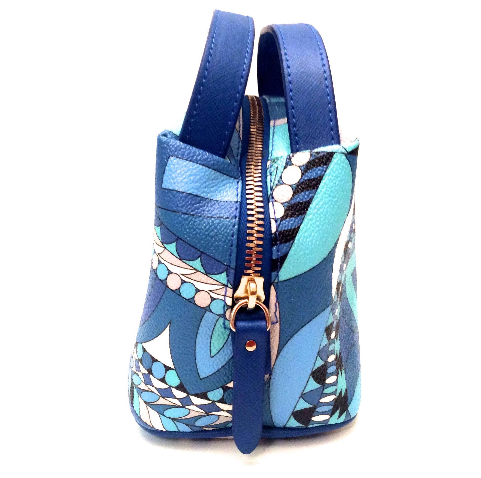 Presented here is a gorgeous mini handbag from Emilio Pucci. The bag is a small little top handle bag that has a zippered top. The pattern is comprised of shades of blue, white, black and gray. The zipper is gold tone with blue leather. The top