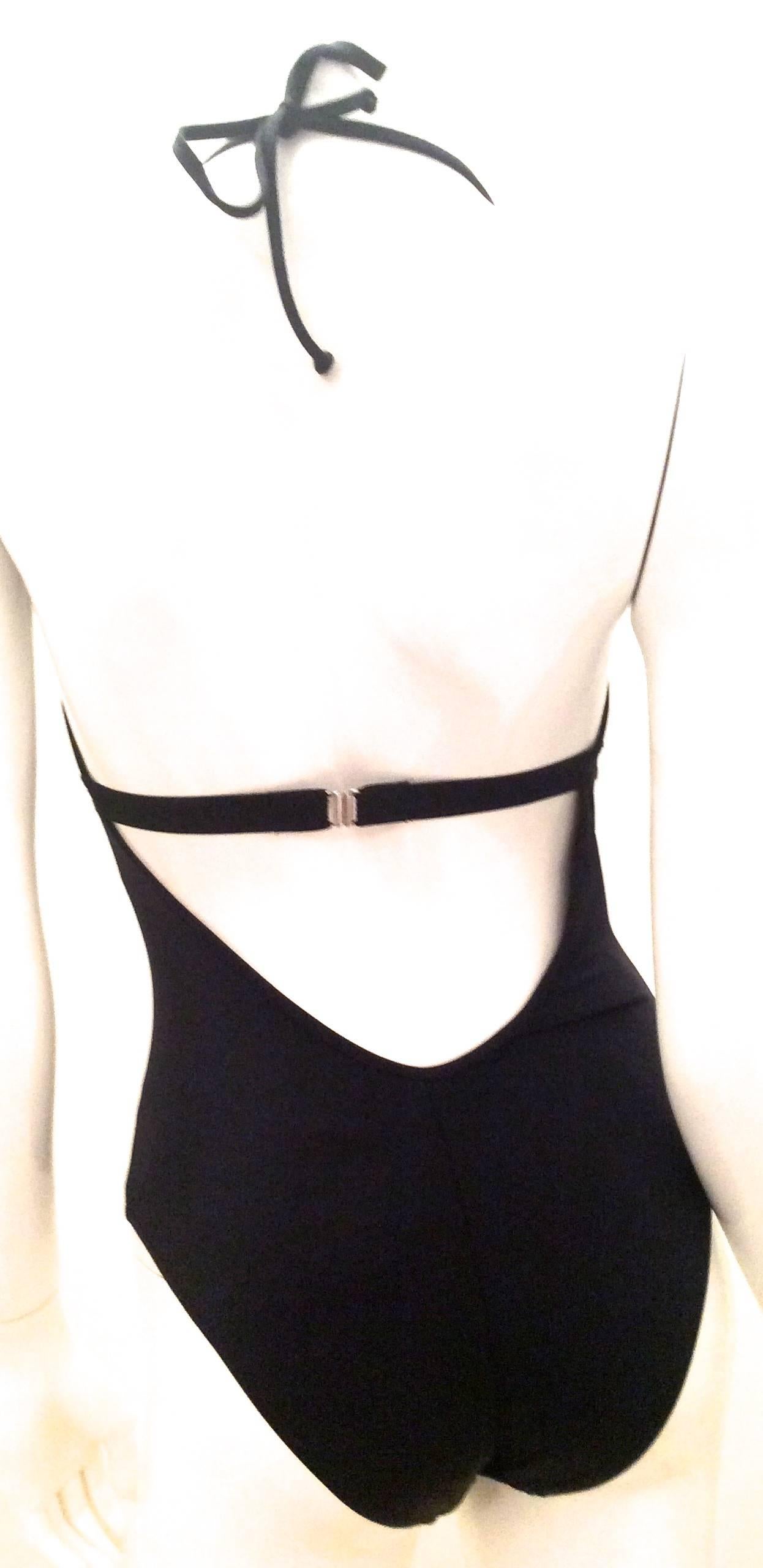 Presented here is a black Moschino swimsuit. There is an elastic band below the breasts suit for support. The back of the swimsuit is cut low to allow the back to be displayed nicely. Through the opening on the back, there is a singular elastic