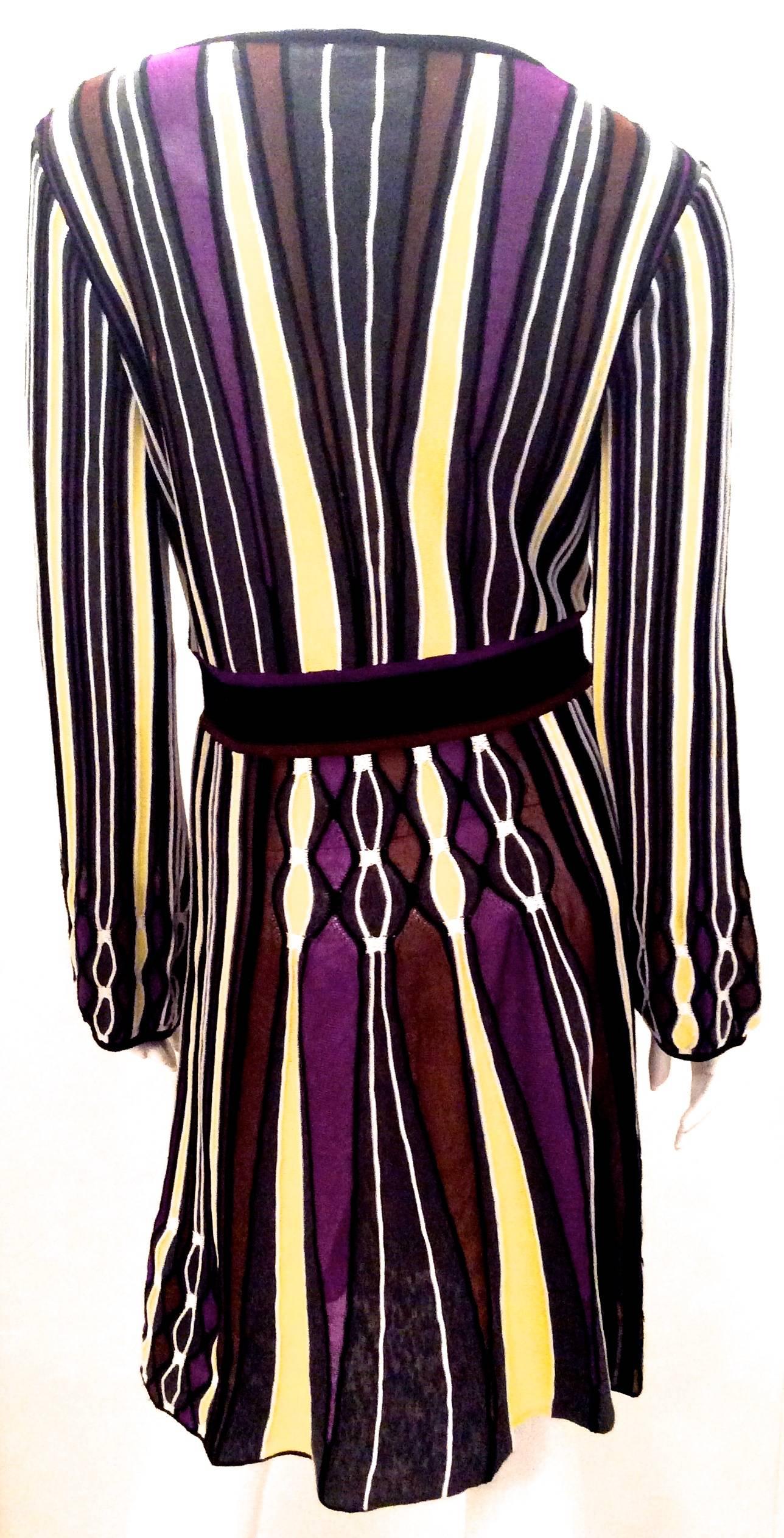 Presented here is a magnificent dress from Missoni. The dress is a series of vertical yellow, gray, black, purple, and brown lines of different sizings with a thick horizontal black line around the waist. The dress has long sleeves. There is a V