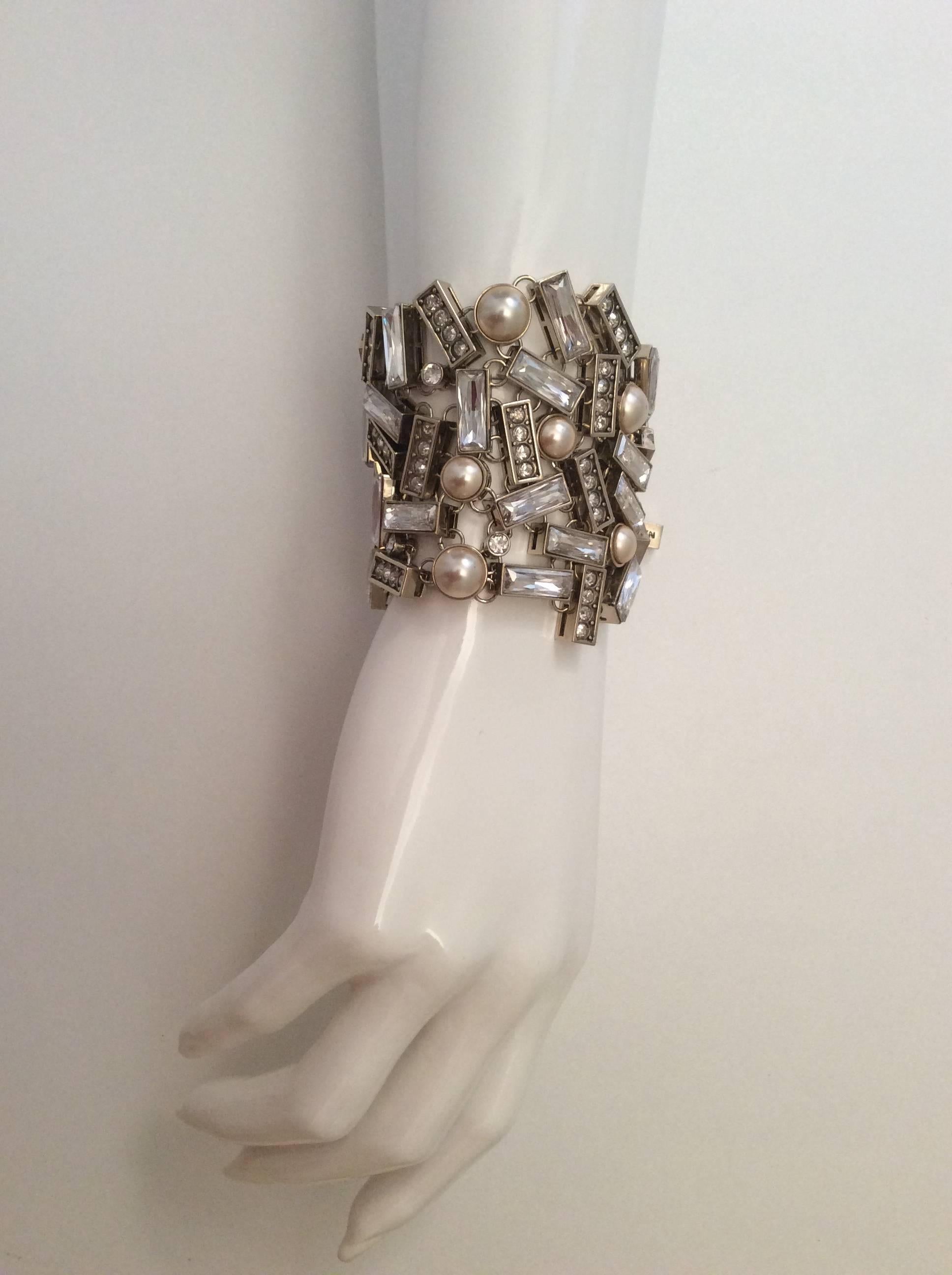 Presented here is a magnificent runway bracelet from St. John. The bracelet is a series of rhinestones and pearls encased in rectangular and circular shapes. There are long baguettes and circular rhinestones. The bracelet has a silver tone clasp