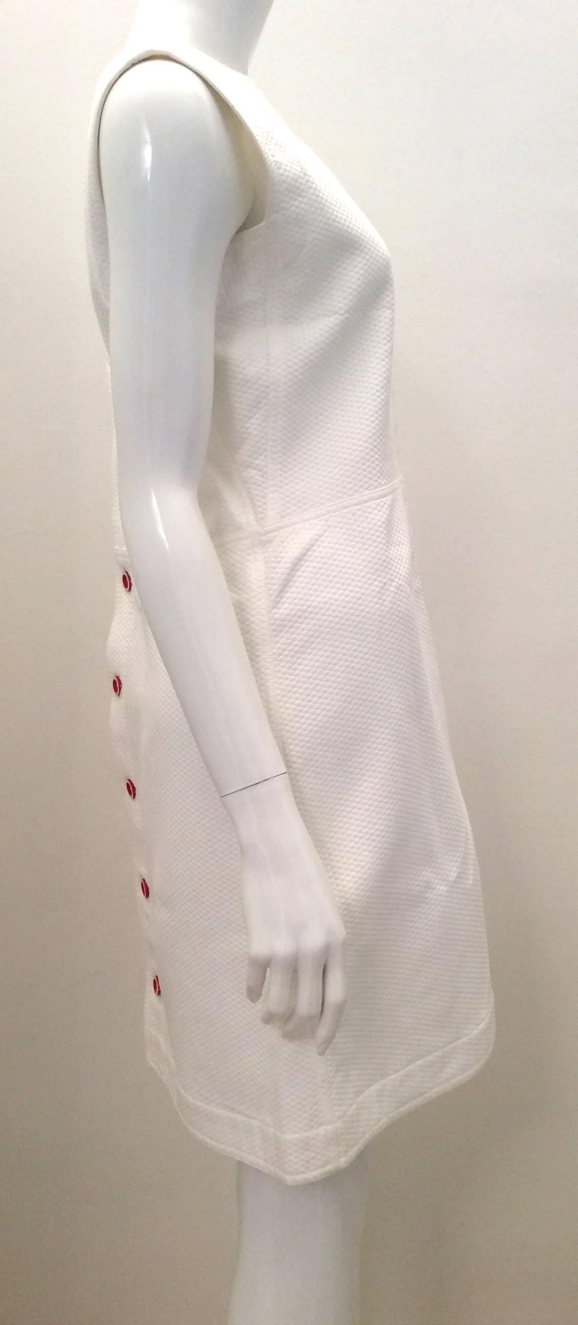Presented here is a gorgeous dress from Courreges. The dress is made of 100% cotton. The dress is a simple cut that buttons up the back of the dress. The buttons on the dress are red. There is a red embroidered Courreges logo on the front of the