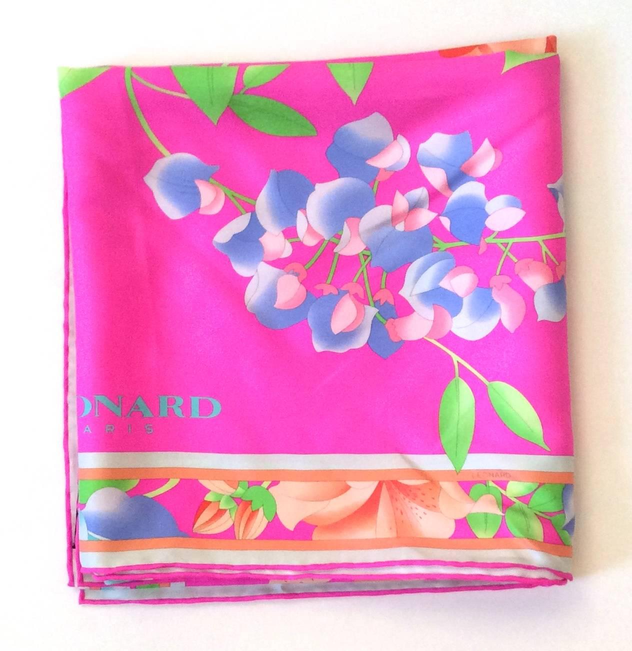 Presented here is a silk from Leonard. The scarf is comprised of a vibrant bright magenta background. In the foregrounded of the scarf, there are bright colored flowers comprised of shades of blue, red, green, and pink. There are brightly colored