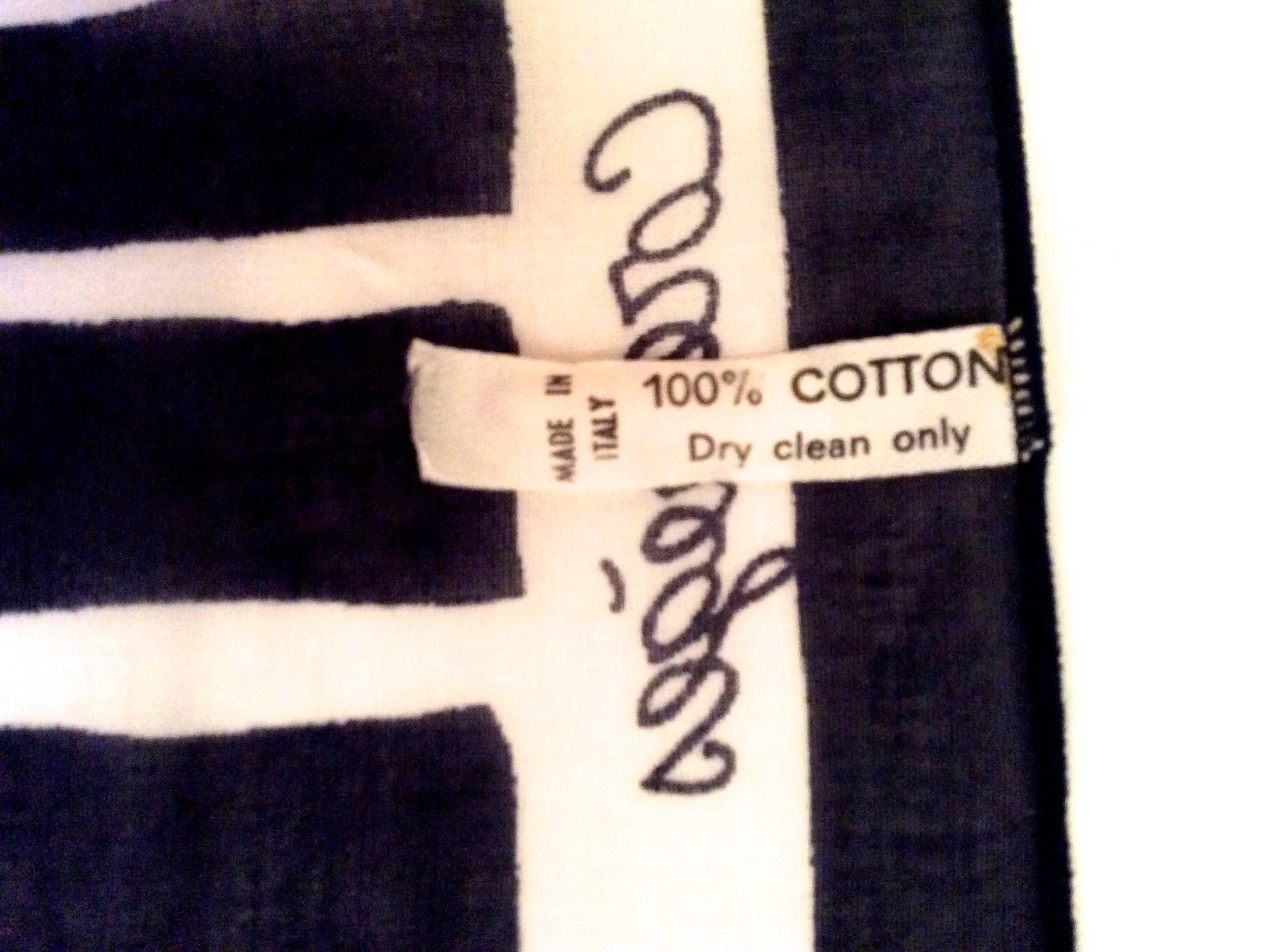 Presented here is a beautiful cotton scarf from Courreges. The scarf is a series of blue stripes against a solid white background with a navy blue and white border around the scarf. Embedded inside the white portion of the border is the name