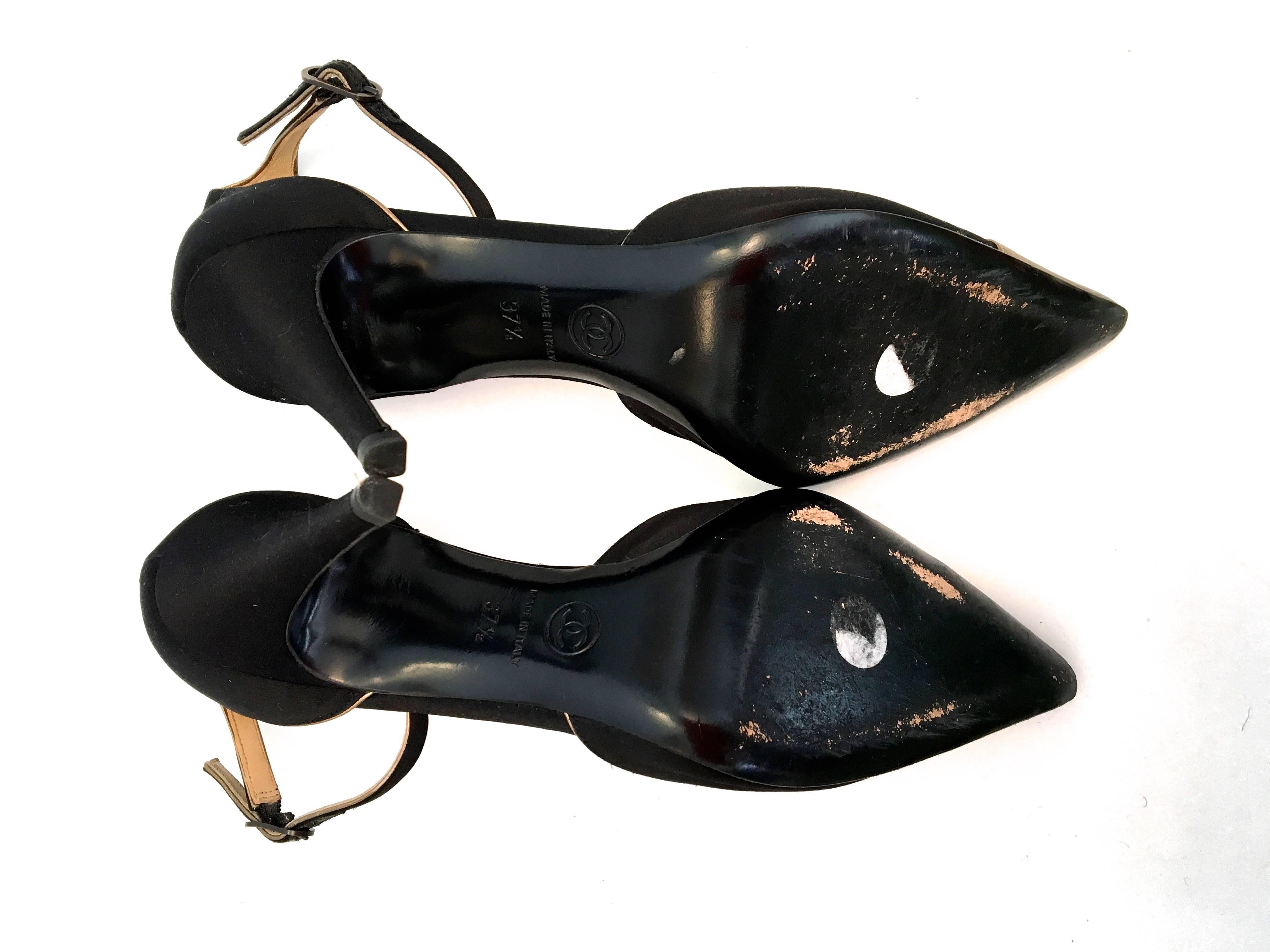 Presented here is a beautiful pair of Chanel heels. The heels are black satin with gold leather trim on the exterior and interior of the shoe. They are a size 37.5. The shoes have a 3.4 inch heel. The total length of the shoe is 10.5 inches. The