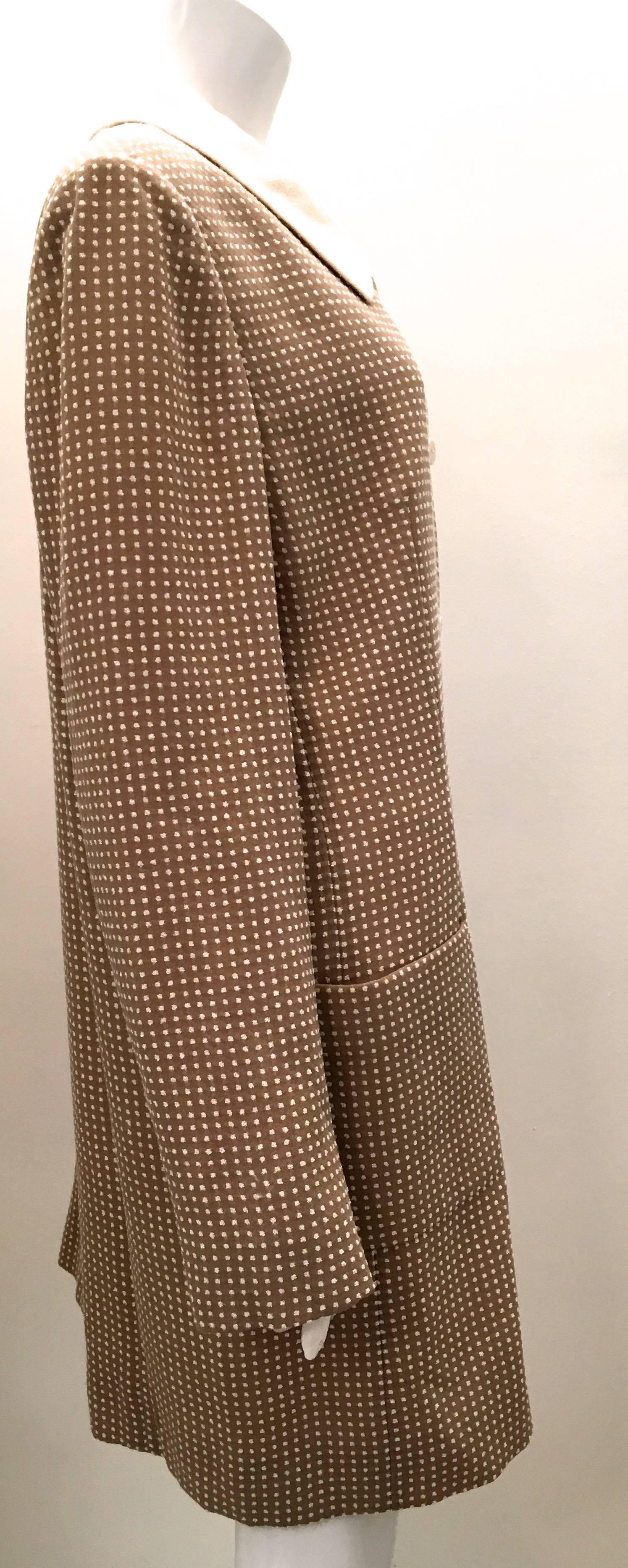Presented here is a Bill Blass coat from the 1970's. The coat is beige on the exterior with small white polka dots patterned throughout the outside of the coat. The collar is white. The inside of the coat is entirely lined in white silk. There are