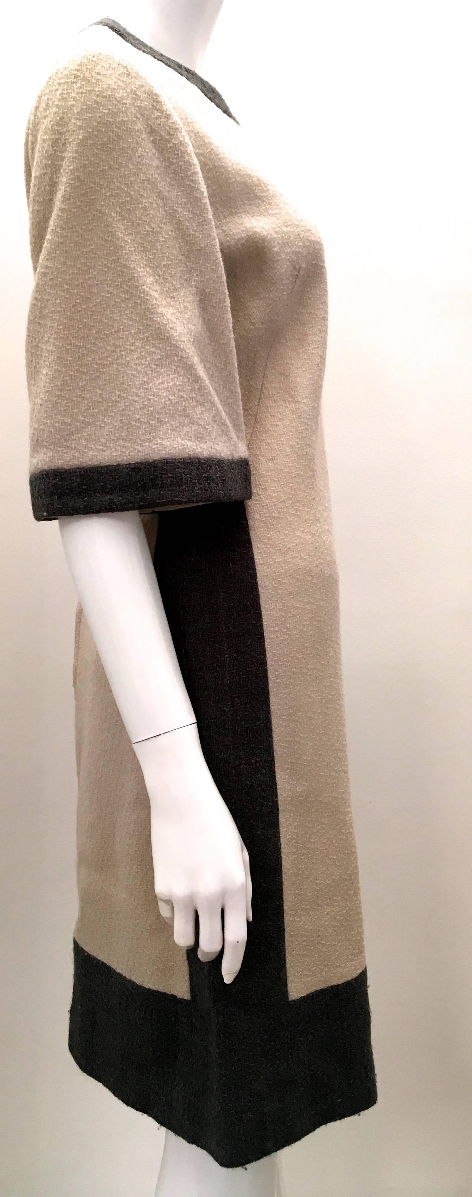 Presented here is a timeless and classic dress by Alison Ayres from the early 1960's. The dress is a creamy beige wool on the front and back with a charcoal gray trim in the same wool fabric around the edges of the dress framing the dress. The