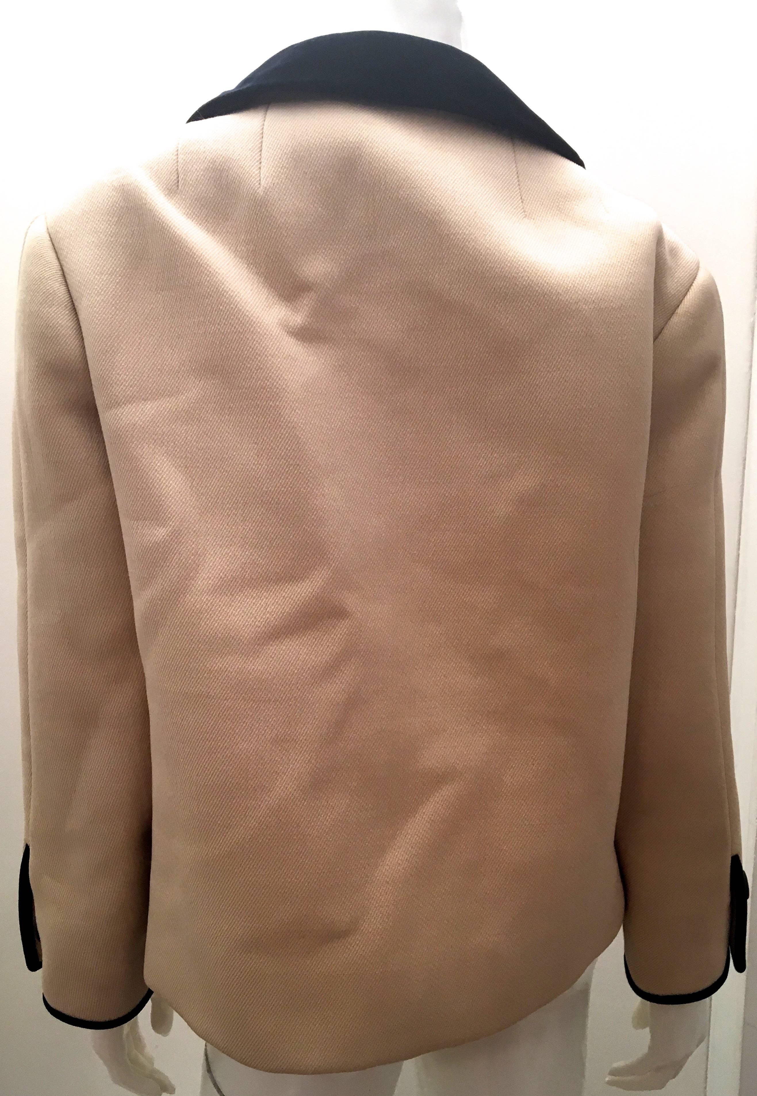 Presented here is a gorgeous 1960's coat from Norman Norell of New York. The coat is a beige cream color with dark navy blue trim throughout the jacket. The coat is double breasted and has large dark navy blue buttons on the front. There are two
