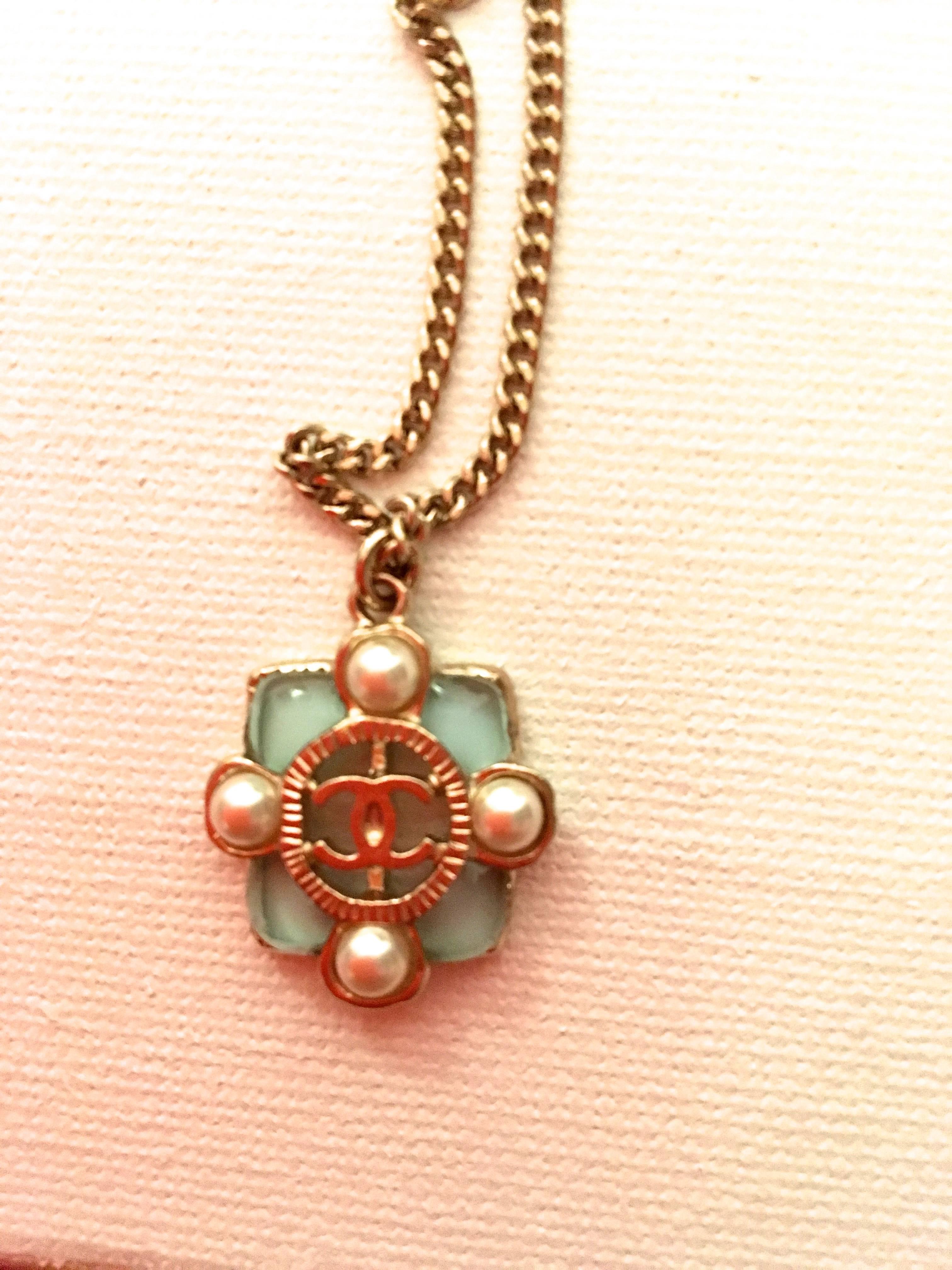 Presented here is a new Chanel medallion necklace from the 2015 collection. The medallion is comprised of a square medallion with a pearl on each side of the square. On each corner of the medallion there is a gripoix stone that is light blue. The