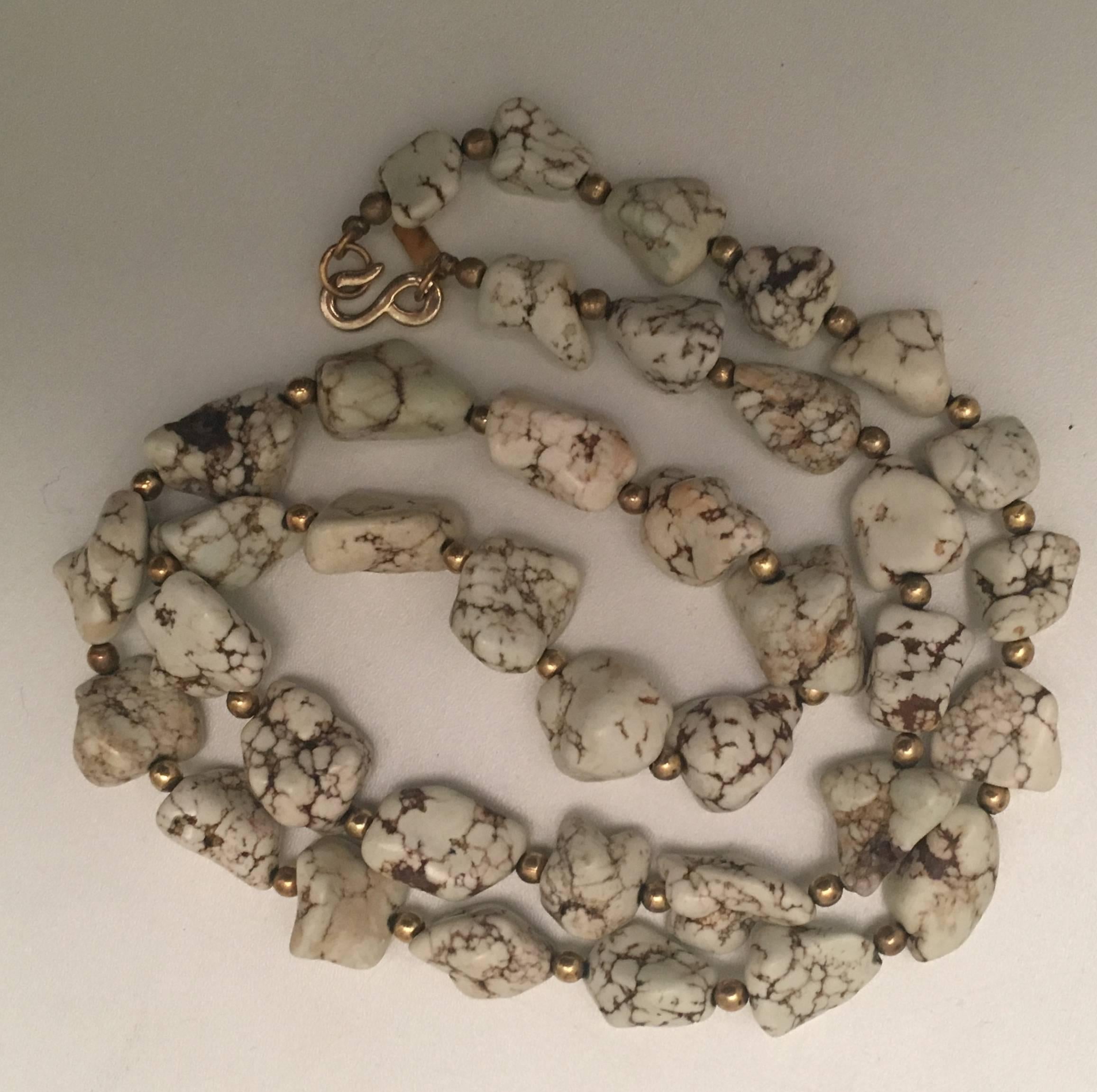 Presented here is a white turquoise stone necklace from Kenneth J. Lane. The necklace is comprised of white turquoise stones threaded onto a necklace with gold tone metal beads in between each stone. The necklace closes with a gold tone metal hook