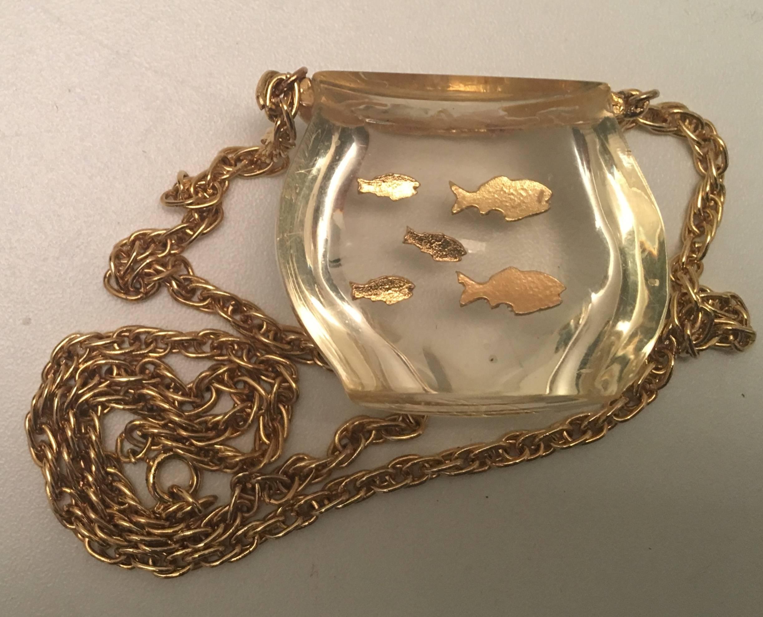 Presented here is a vintage lucite fish bowl necklace from the 1970's. The necklace is comprised of a beautiful lucite fishbowl containing five swimming fish. There is a gold tone metal chain attached to the fish bowl necklace. This wonderful