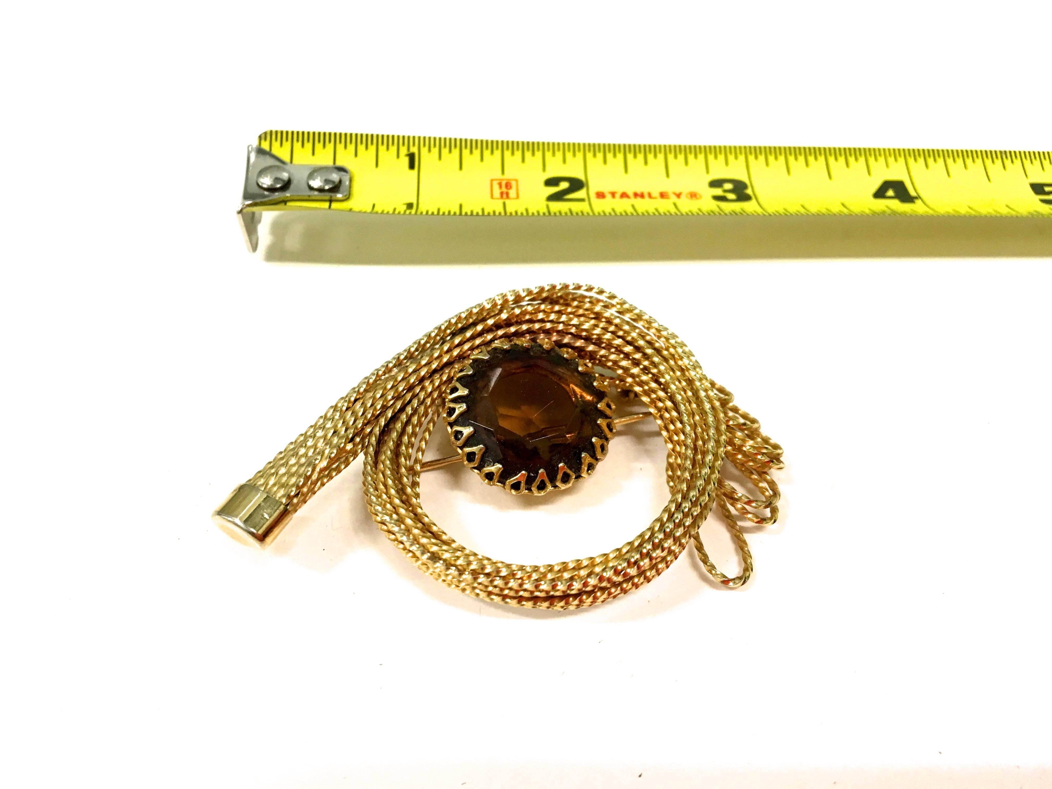 Presented here is a beautiful 1950’s gold tone metal brooch. At the center of the brooch, there is a dark amber colored gem stone that is fastened to the pin with triangular rivets. There is a clasped pin on the back of the pin. Surrounding the