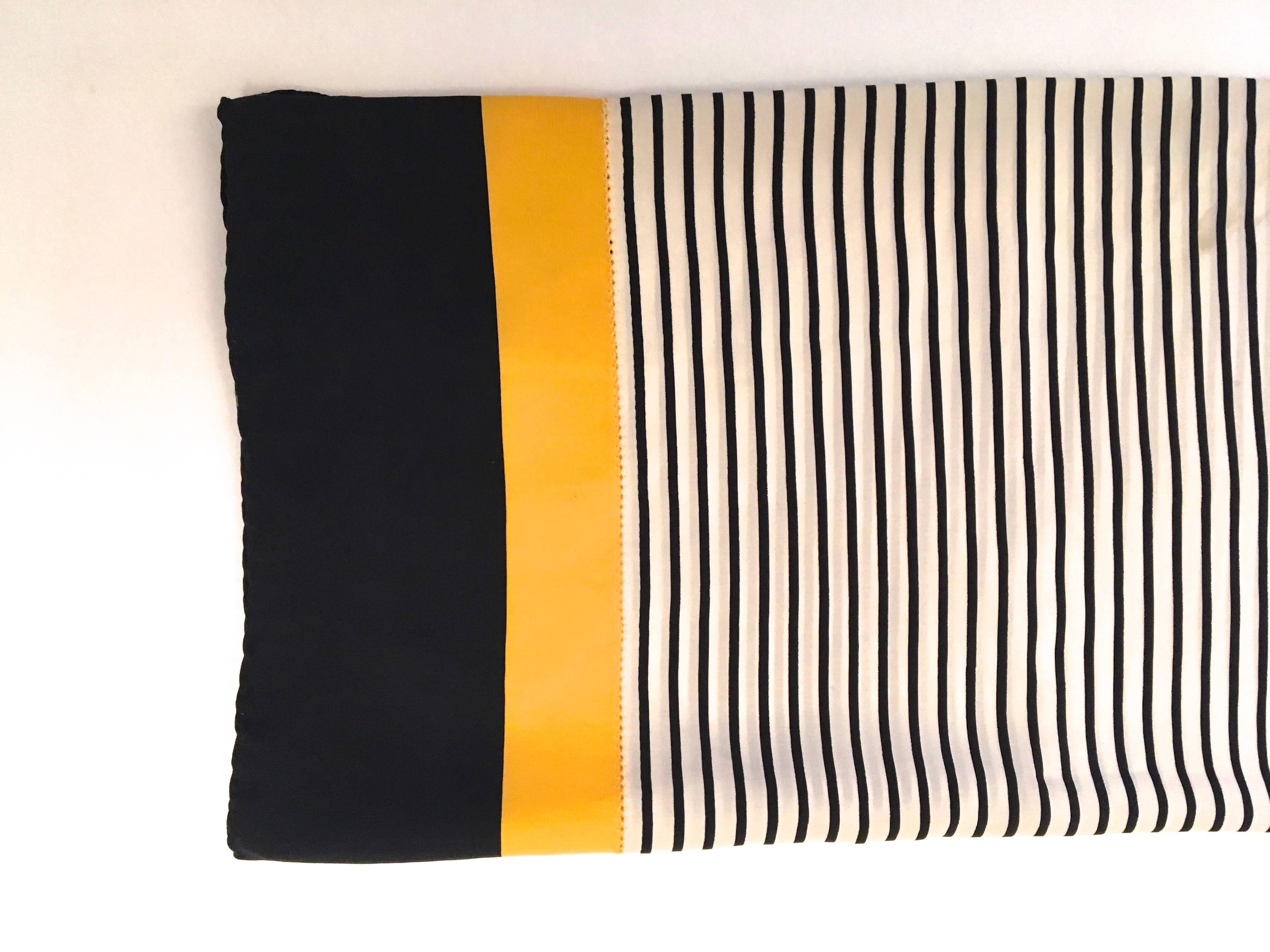 Presented here is a beautiful scarf that is made from 100% silk. The scarf is from the 1980's. The scarf is comprised of a center square of blue  and white lines. The center square is encased by a border of yellow and blue around the exterior of the