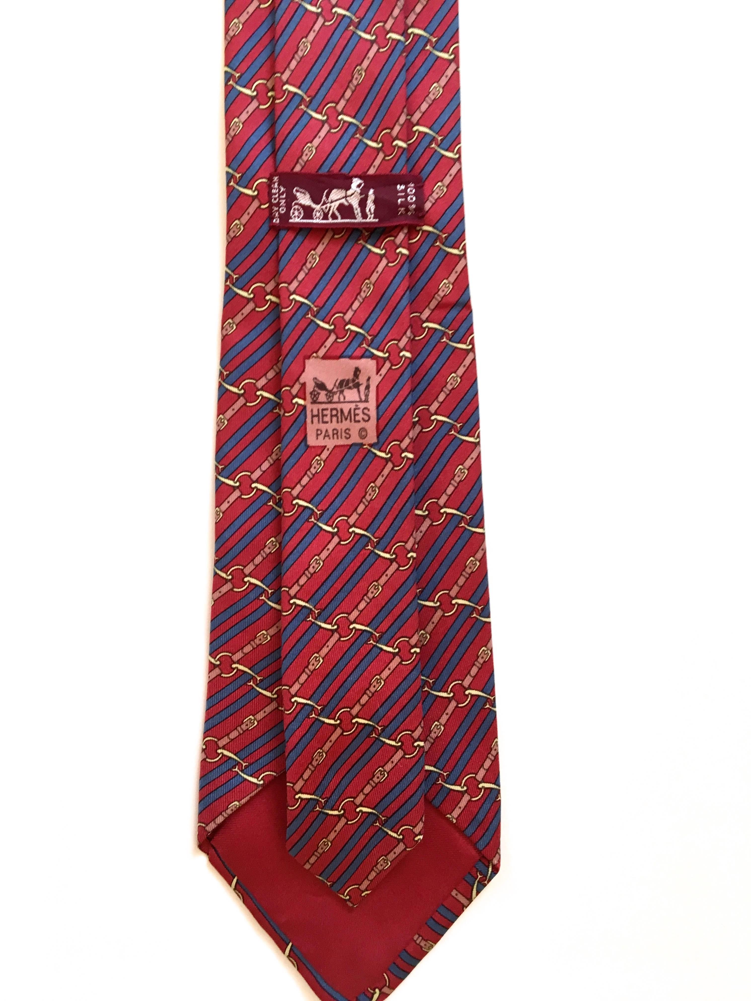 Presented here is a silk necktie from Hermes Paris. This beautiful tie is comprised of a red background with horse stirrups and straps in the foreground. The tie is comprised colors of reds, blues, golds and browns. A beautiful design that is a