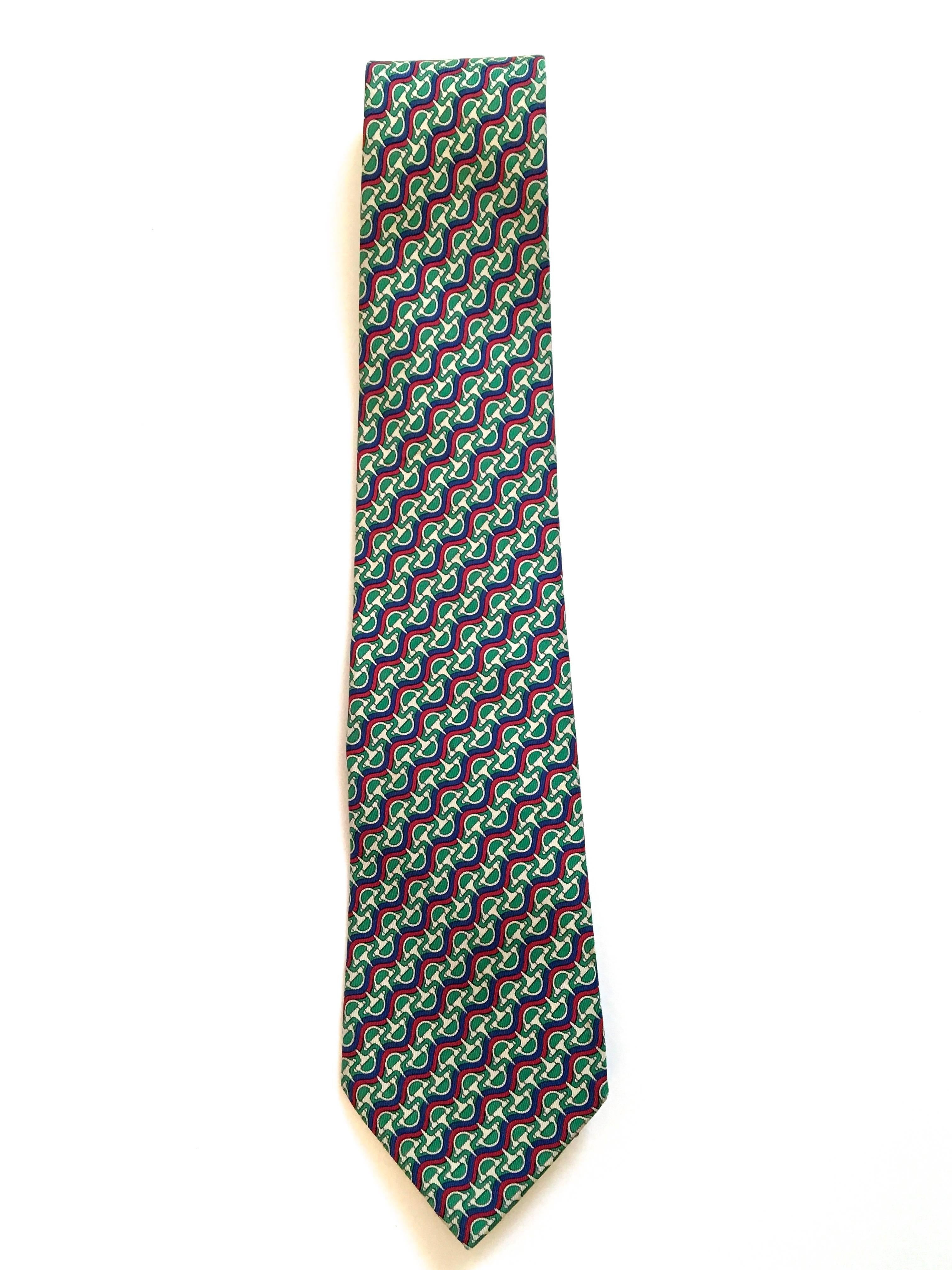 Presented here is a silk necktie from Hermes Paris. The tie is comprised of colors of red, green, gray and blue. The design is a tessellation of horse bits in a beautiful geometric pattern. The combination of discrete shapes and colors make for a