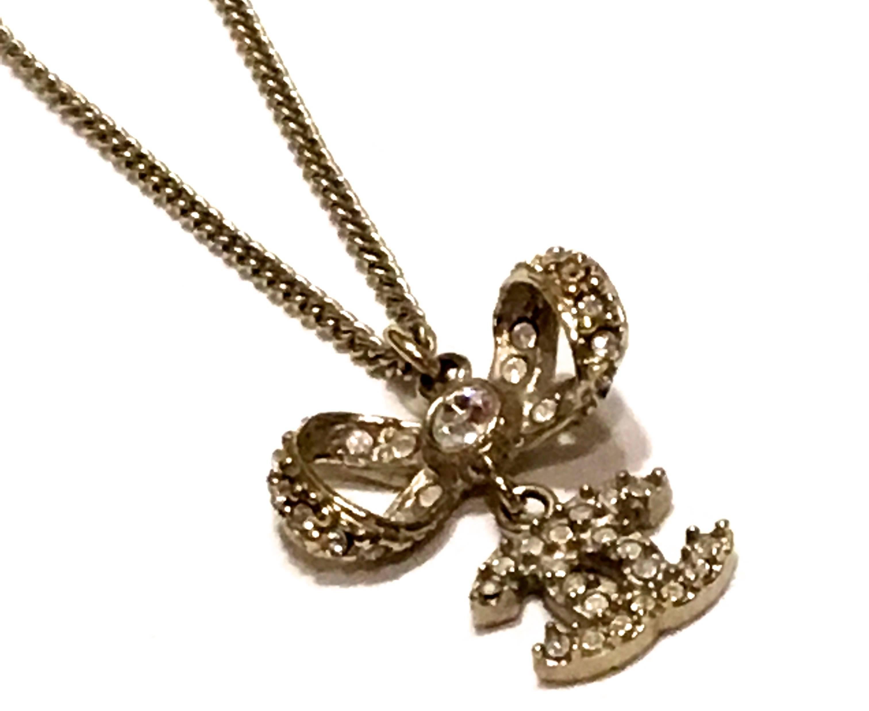 Presented here is a beautiful charm necklace from Chanel. This necklace has a beautiful finely woven gold tone metal chain. On the chain, there is a gold tone metal bow encrusted with clear rhinestones. There is a dangling iconic CC logo linked to