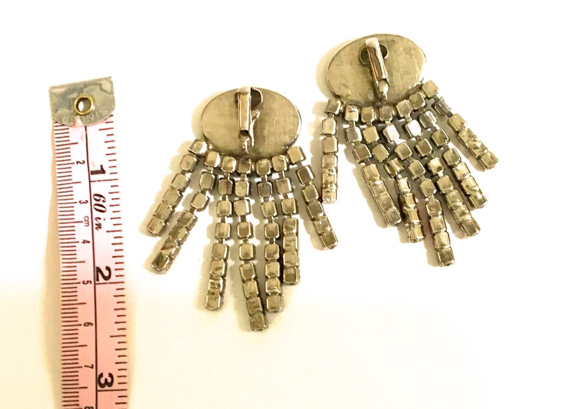 Presented here is a beautiful pair of earrings from the 1950's. The earrings are comprised of oval red stones housed in silver tone metal. Dangling from the oval shapes are white and red rhinestones in stringed lines. The earrings have clips on the