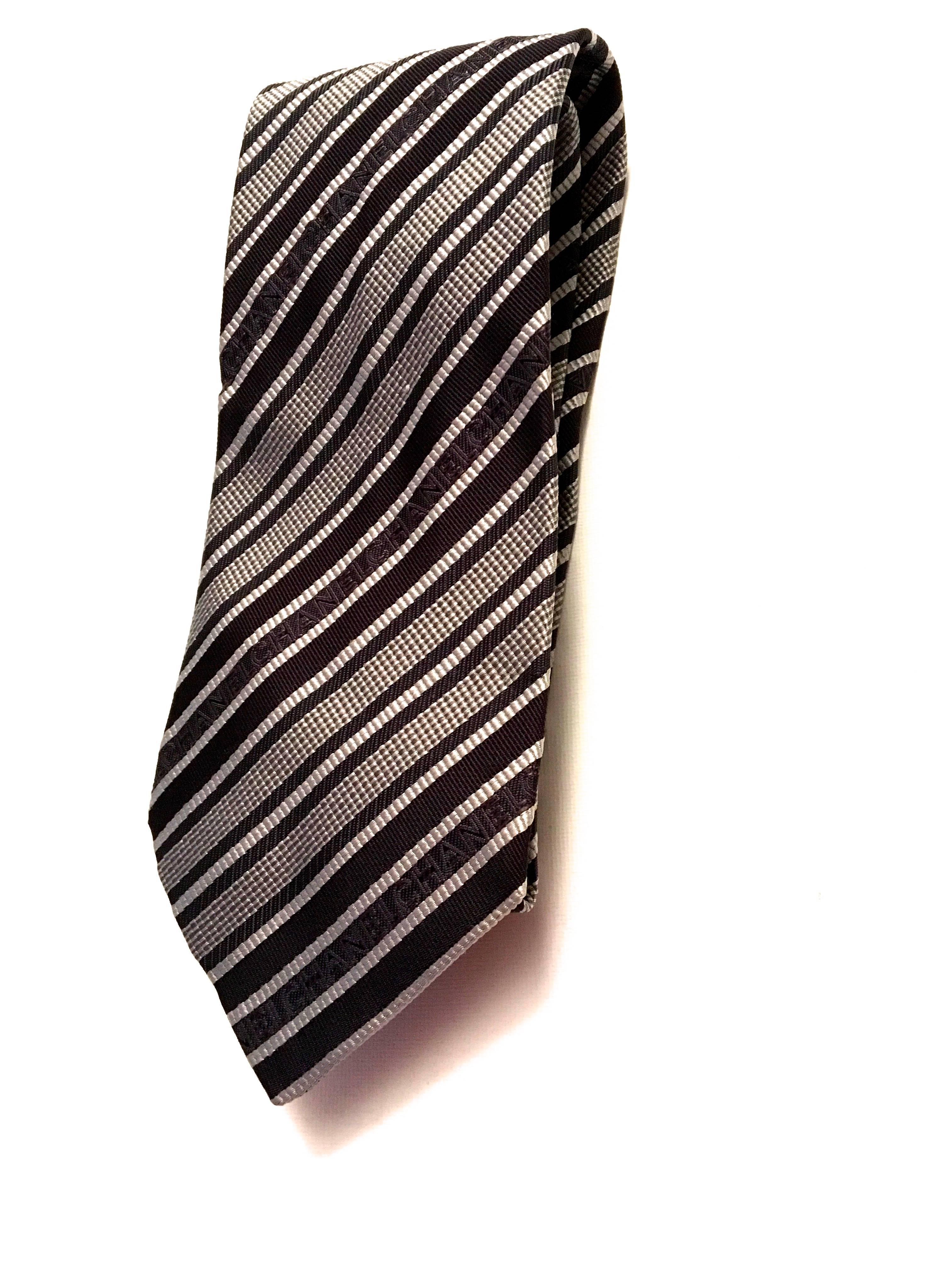Presented here is a beautiful necktie from Chanel’s couture collection. This beautiful tie is made from 100% silk and is composed of silver, gray and black stripes. ‘Chanel’ is written in the body of the tie’s design. This tie has a classic styling