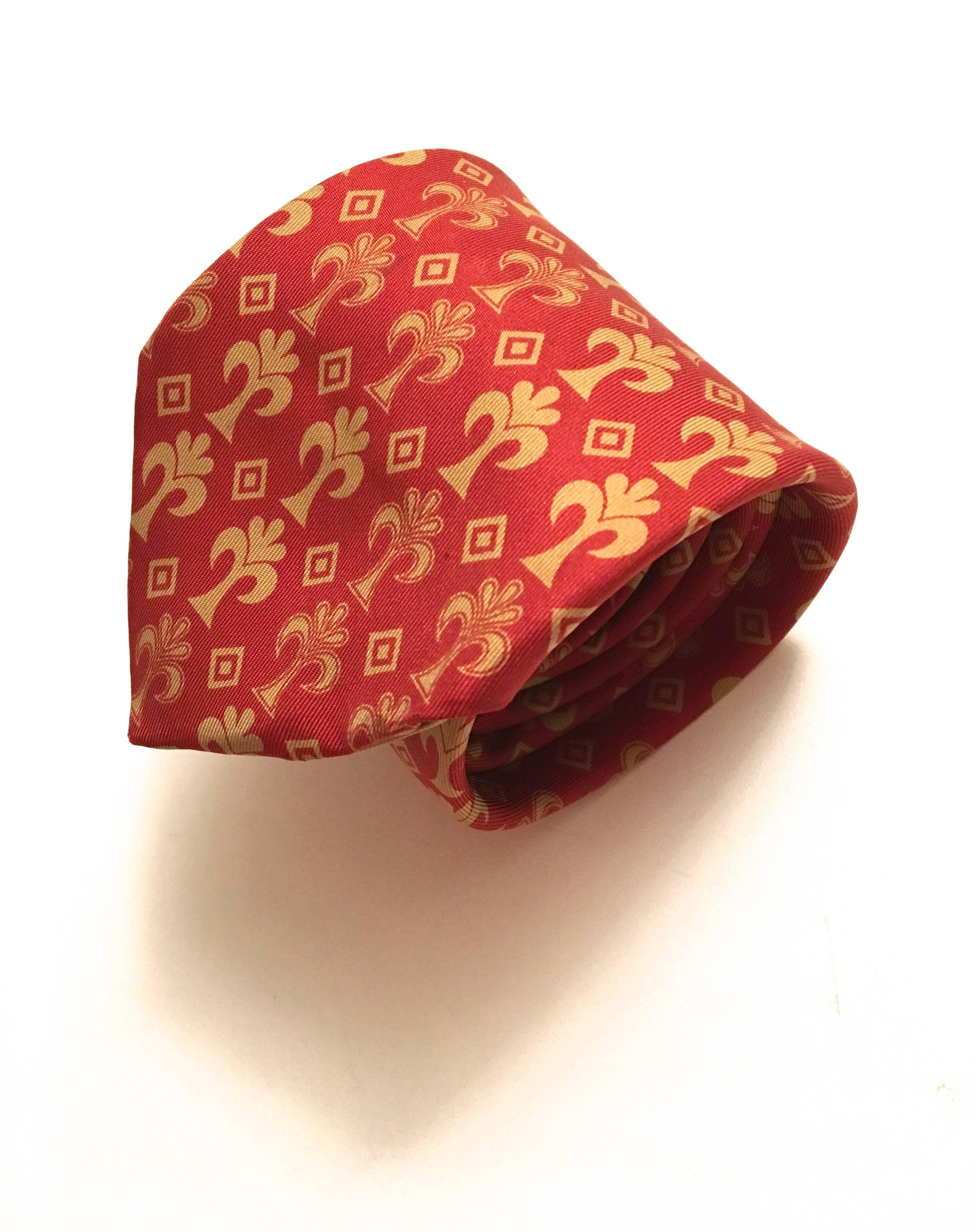 Presented here is a beautiful vintage necktie from Hermes Paris. This beautiful neck tie is a pattern of gold flower-like symbols and squares. The symbols are layered along a solid red background. The tie measures 57 inches. At its wide point, the