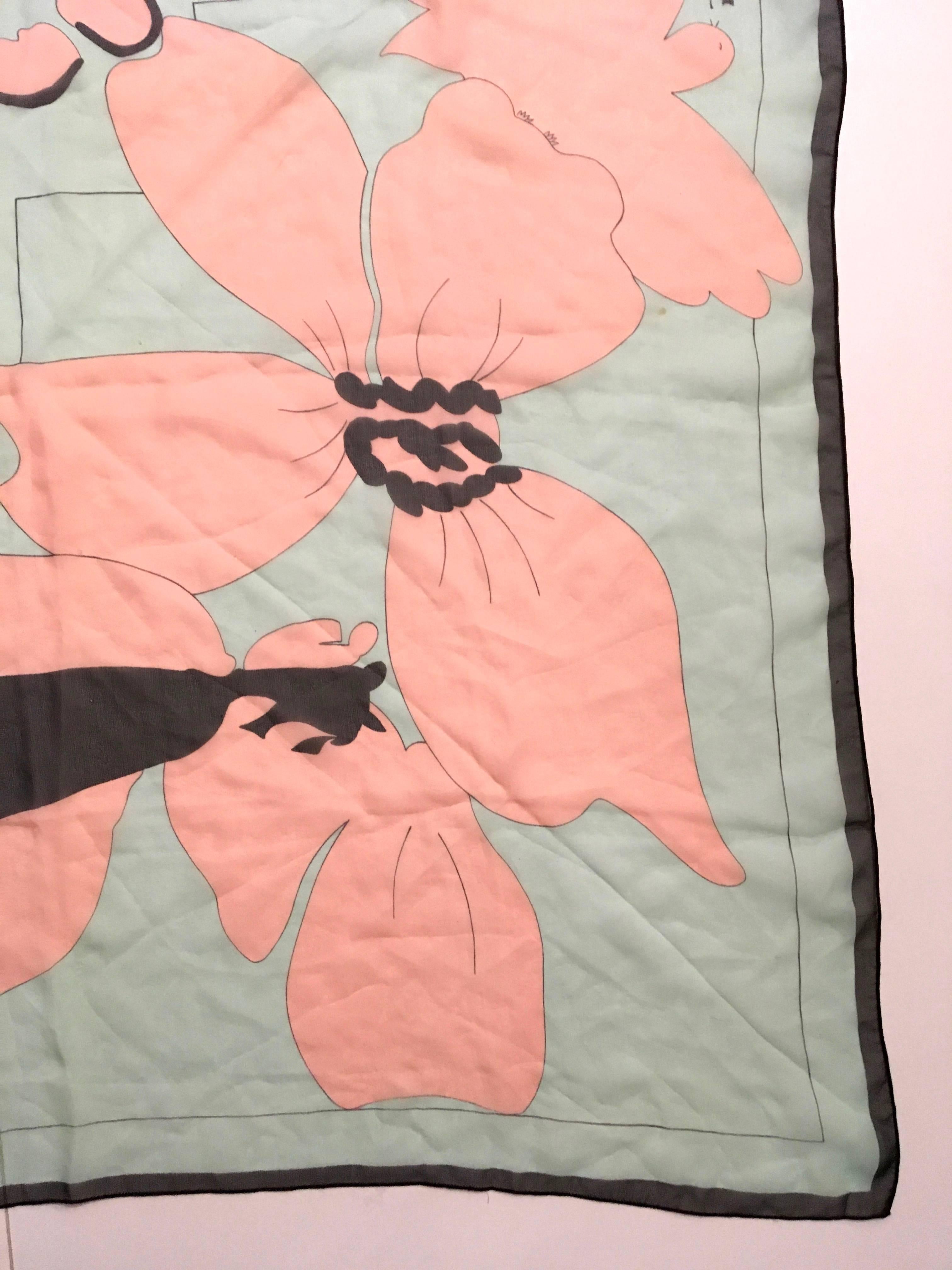 Presented here is a scarf from Courreges Paris. This beautiful scarf is made from 100% silk musselin. The scarf is a floral print and is comprised of pink and black colored flowers against a light blue background. The images are all framed by a