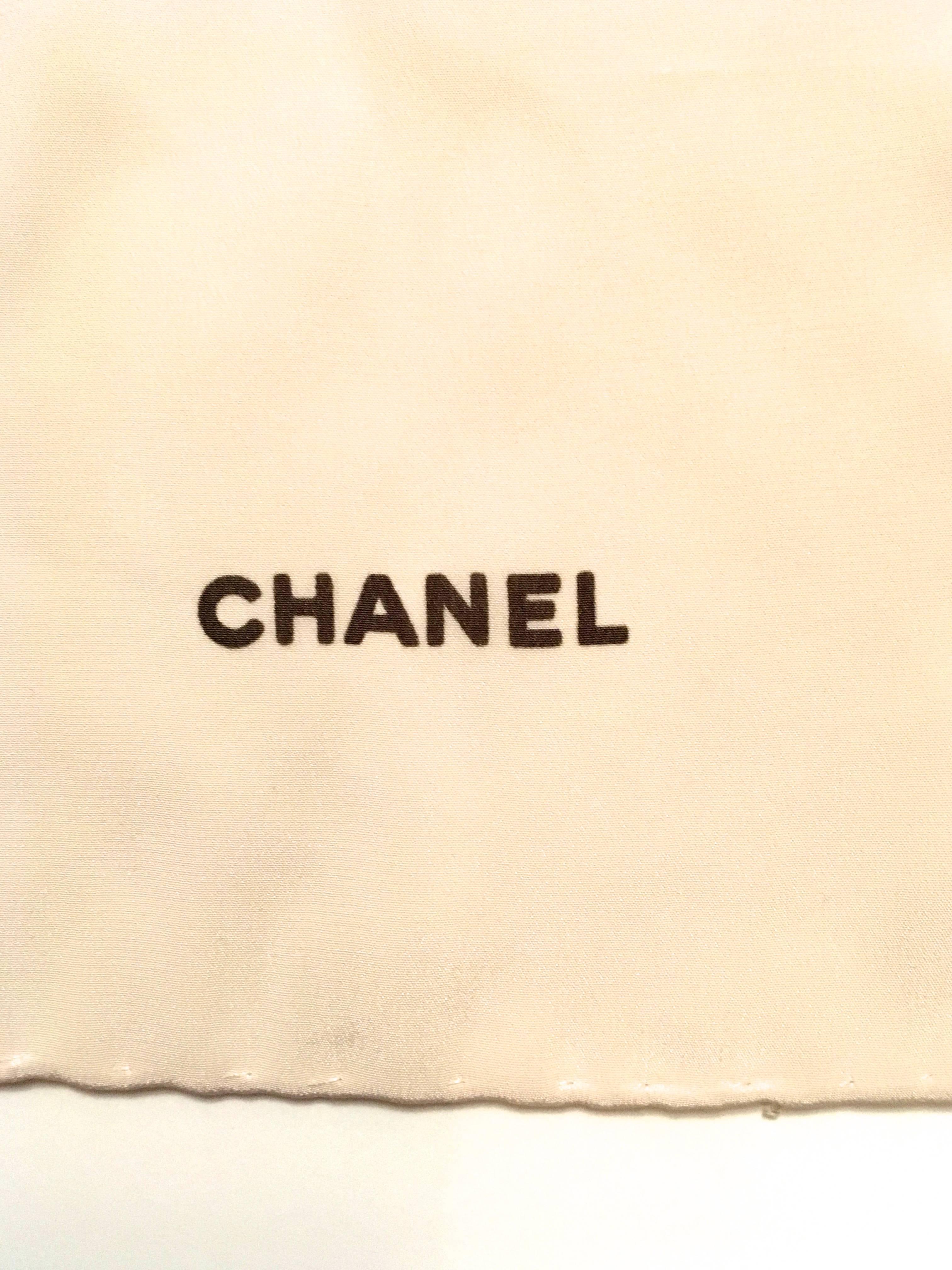 Presented here is a hand rolled silk scarf from Chanel. The scarf is a creamy white background with a floral print of various flowers in shades of pink, red, yellow and white. Accents of green from the leaves are also in the images. The scarf is in