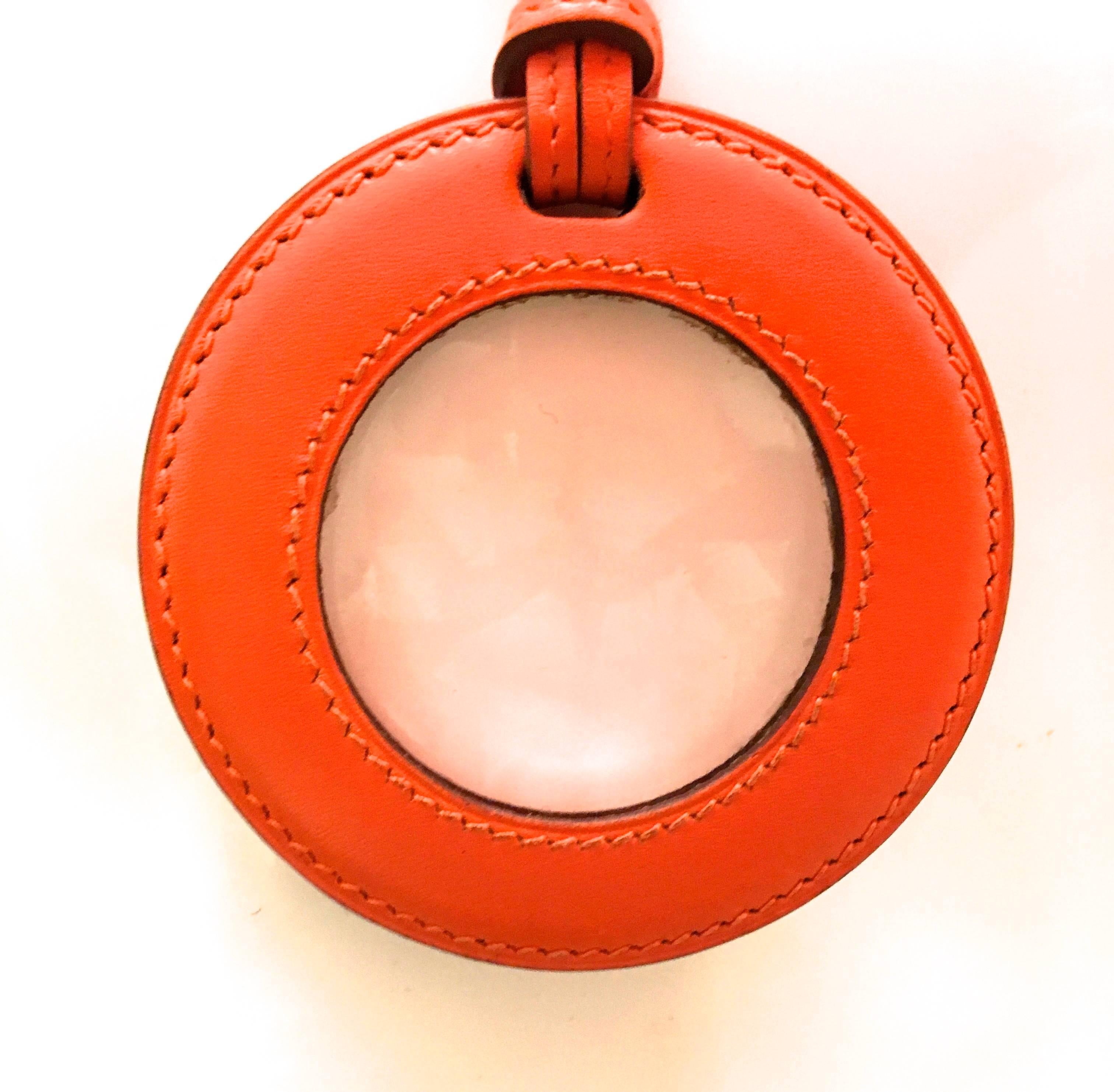 Presented here is a pendant necklace and magnifying glass (loop) from Hermes Paris. The necklace is an orange leather cord attached to a circular leather case. Within the case is a glass magnifying lens. The necklace is both beautiful and functional