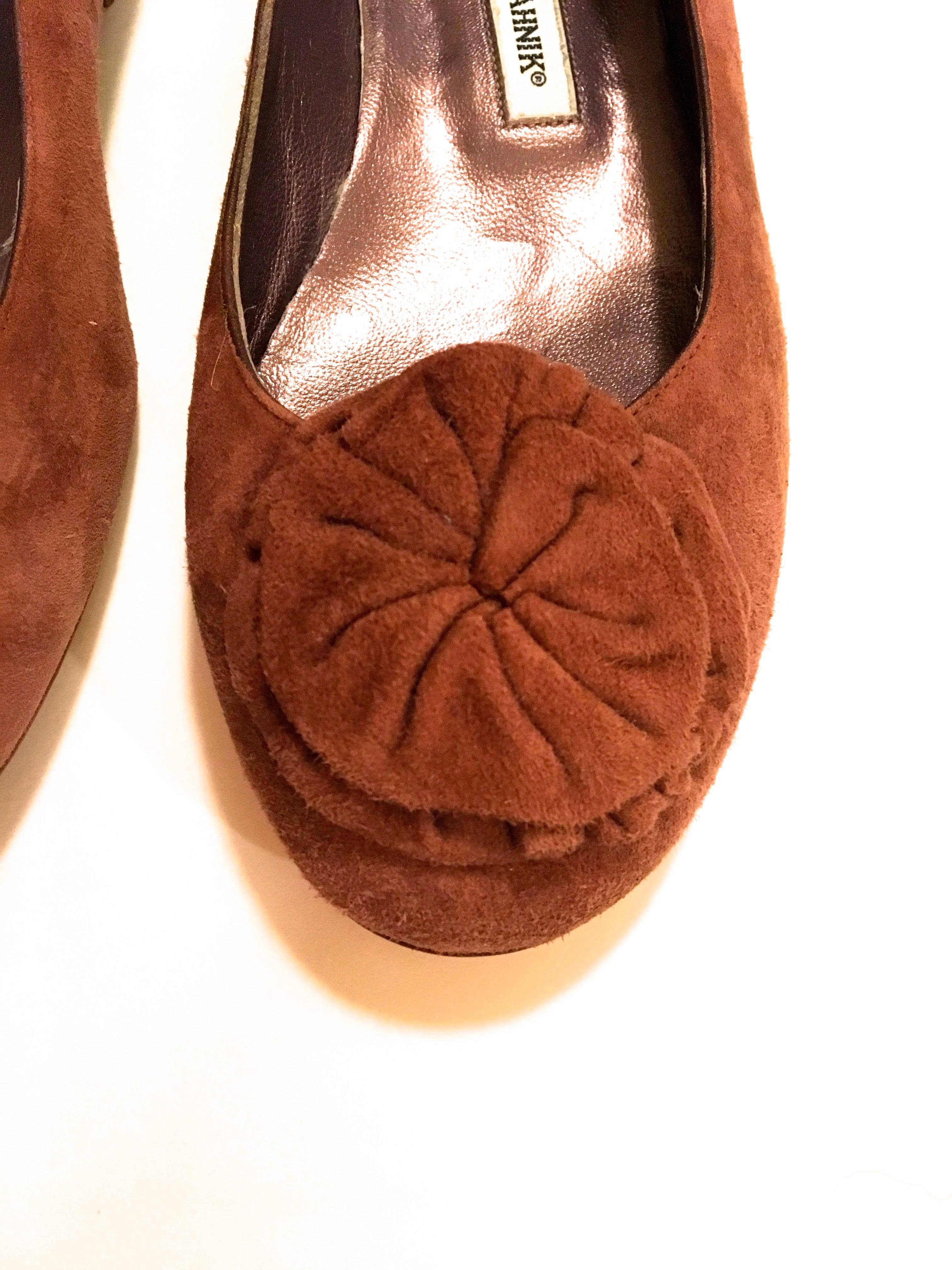 Presented here is a pair of brand new shoes from Manolo Blahnik. This beautiful pair of shoes is comprised of a soft brown suede on the exterior. The shoes are a pair of flats. Each shoe is adorned with a flower on the end of the shoe. The shoes are